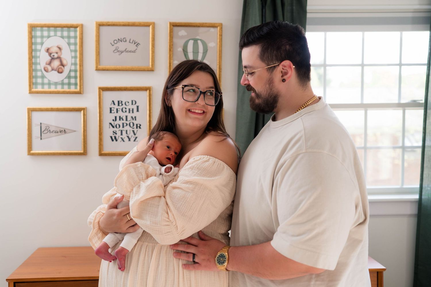 New parents smile lovingly at their newborn baby in a charming nursery with framed wall art.