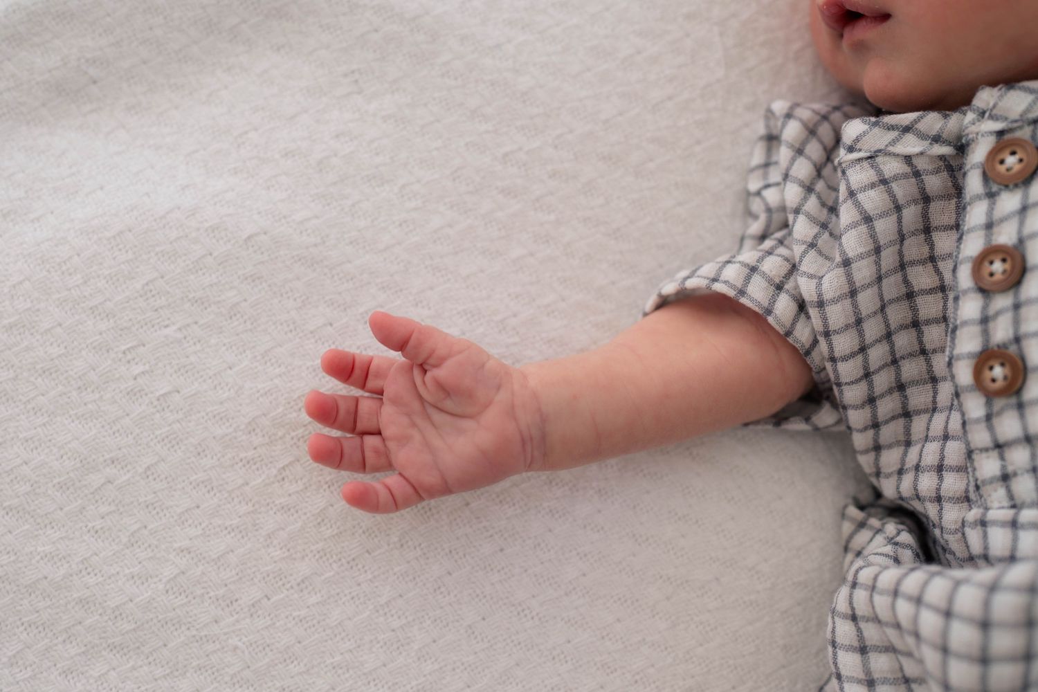 Close-up of sleeping newborn baby hand in plaid outfit on white textured blanket.