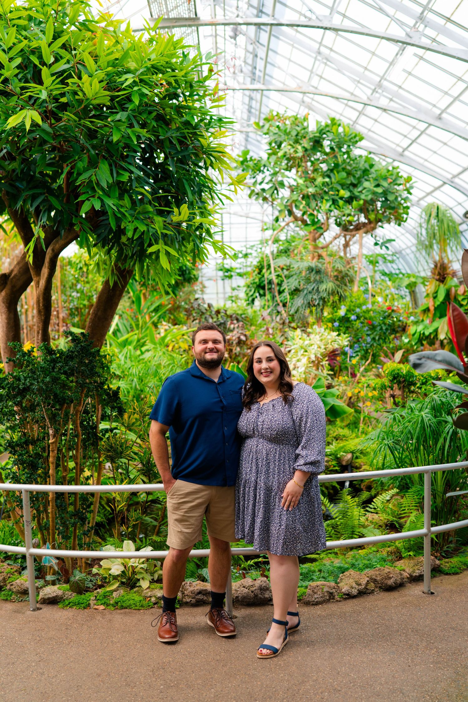 Happy couple posing together on a path inside a tropical botanical garden greenhouse.