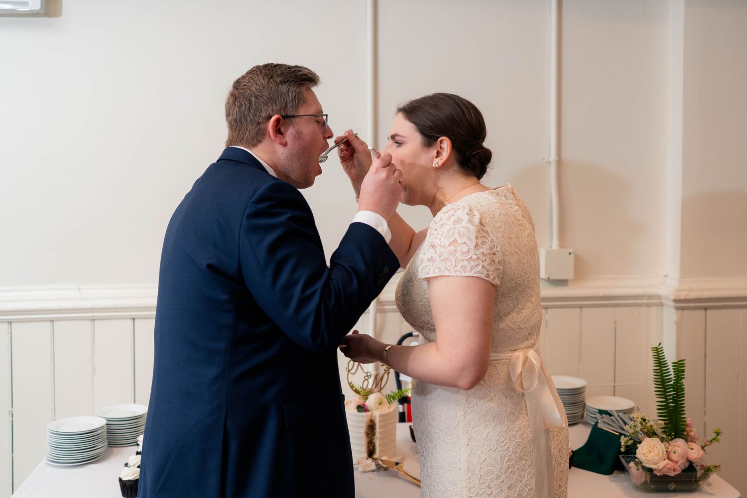 Bride feeding groom a bite of wedding cake during fun cake cutting moment at reception.