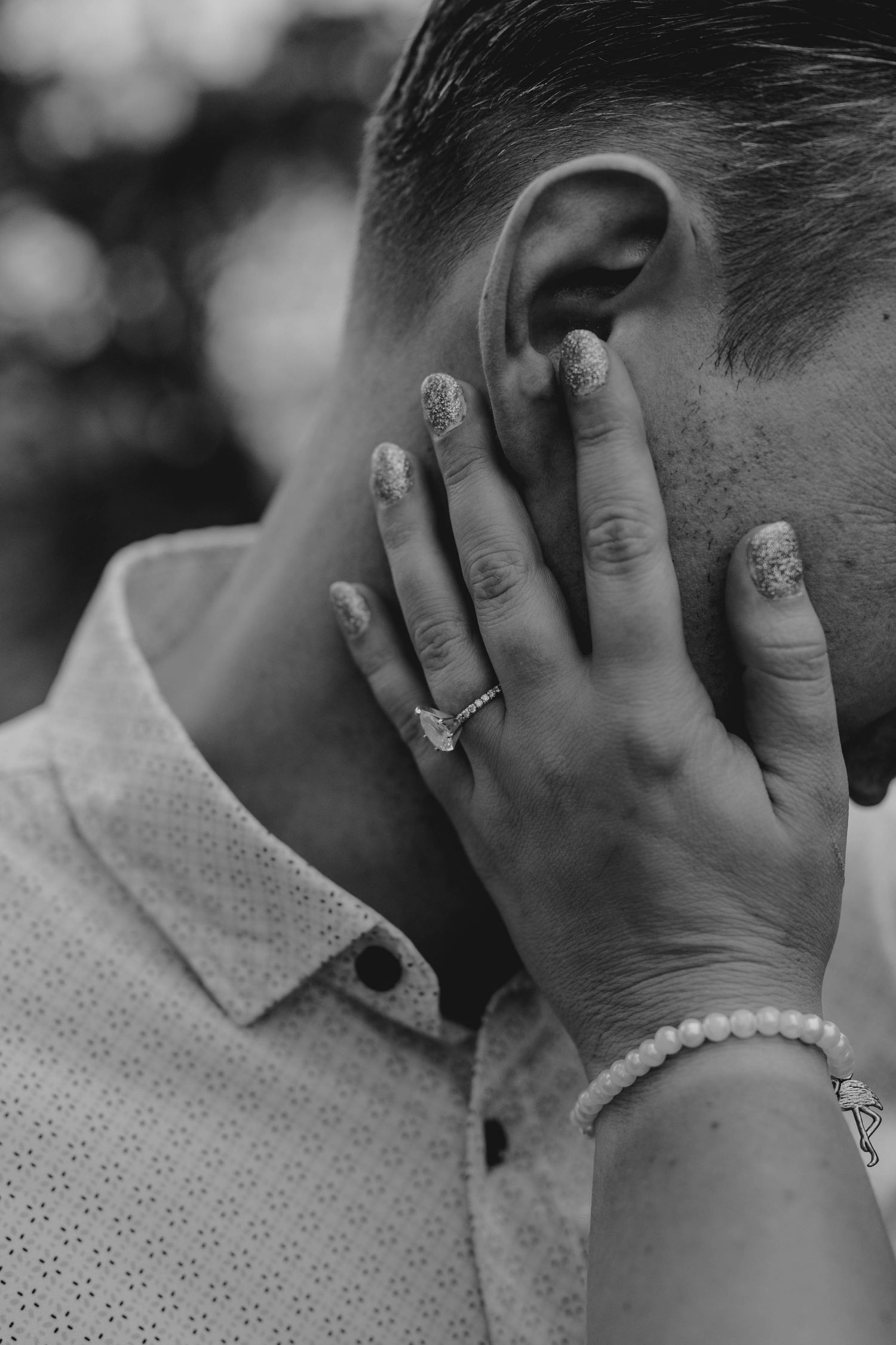 Black and white close-up of a womans hand with engagement ring and pearl bracelet touching a mans face.