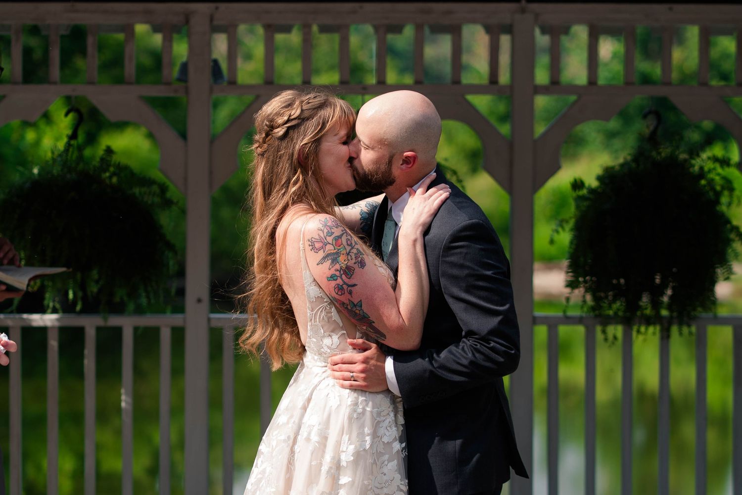 Bride and groom sharing first kiss at outdoor wedding ceremony near decorative white gate.