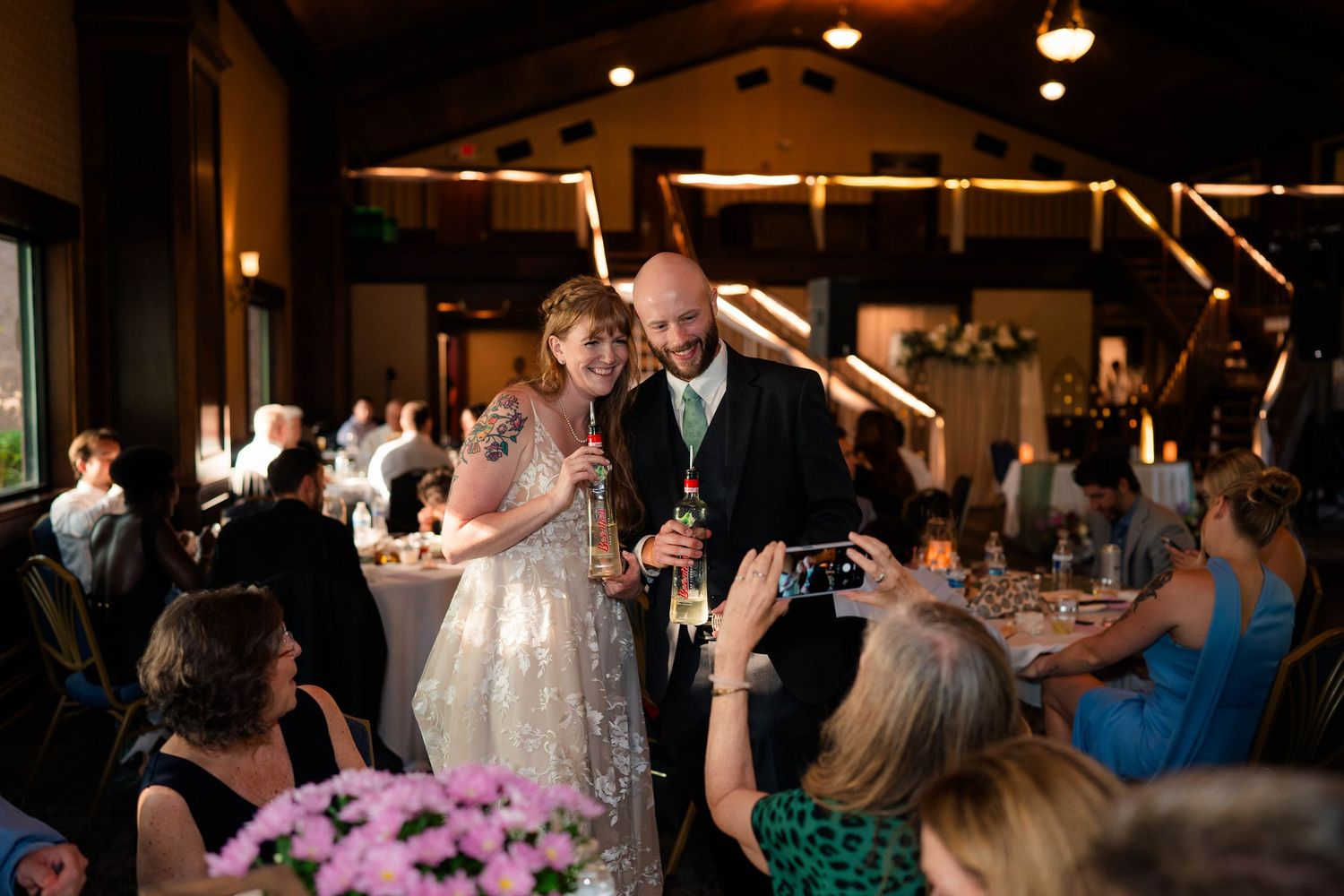 Bride and groom smile together holding microphones during their indoor wedding reception toast.