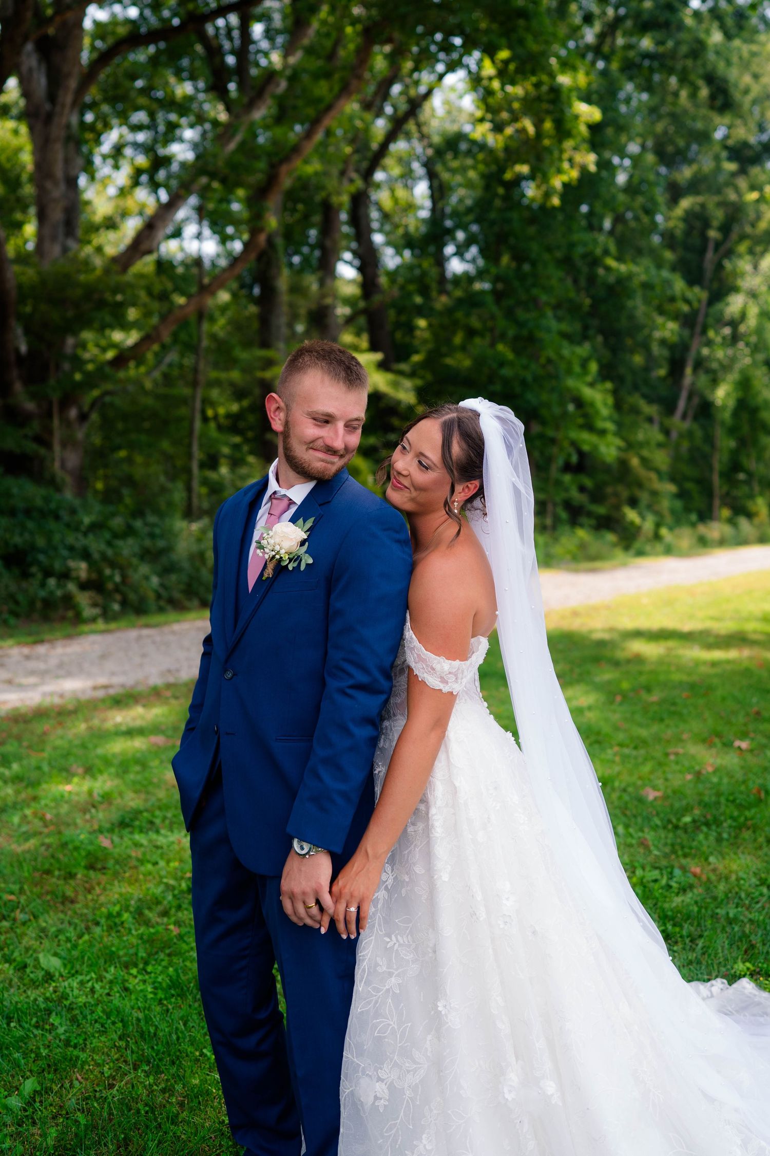 Bride and groom share a romantic moment holding hands outdoors surrounded by lush green trees.