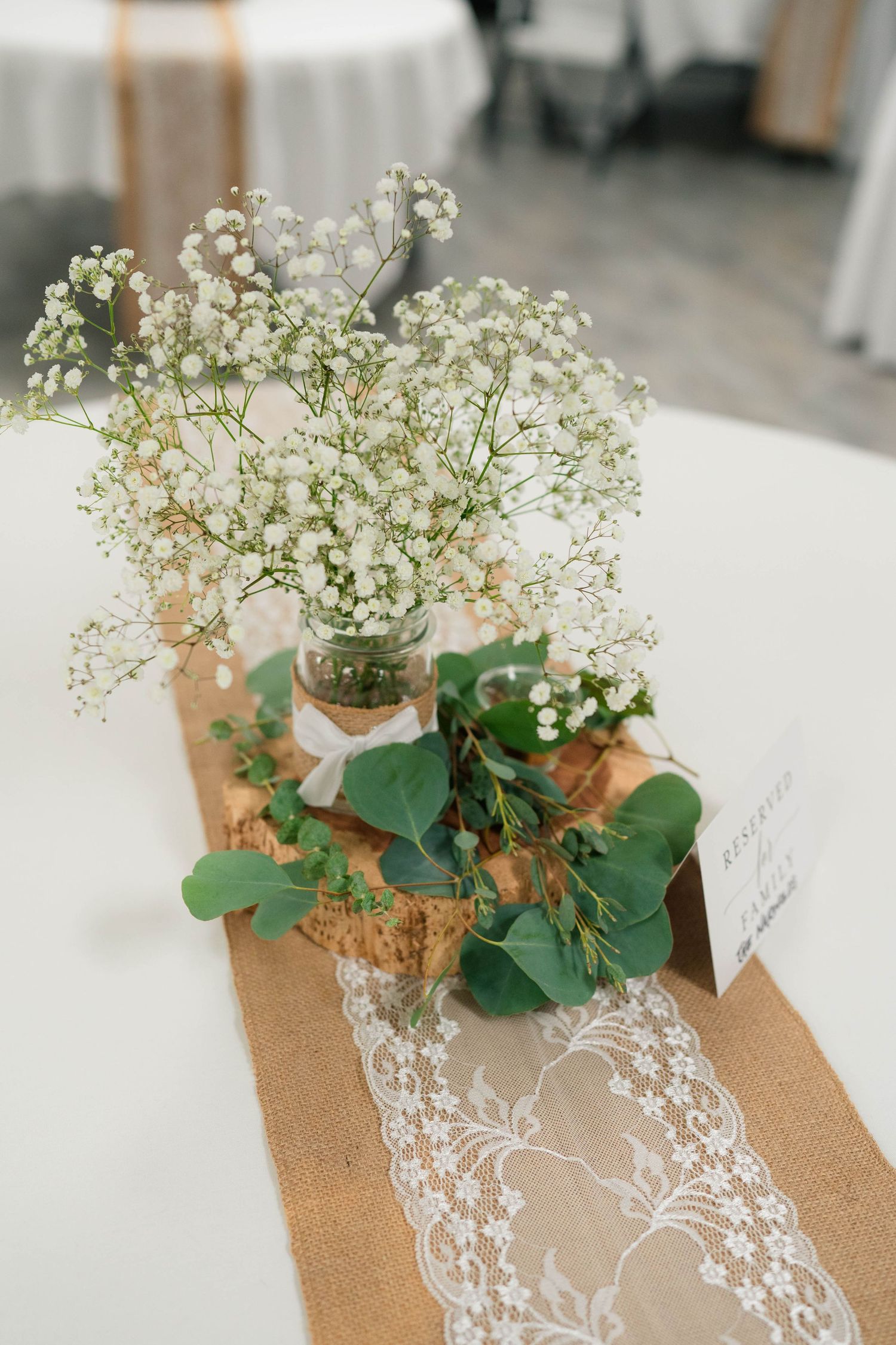 Rustic wedding centerpiece with baby's breath in glass vase on burlap and lace table runner.