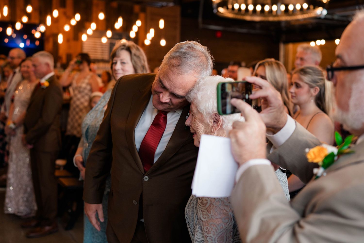 Emotional father of the bride moment captured during wedding ceremony with guests photographing nearby.