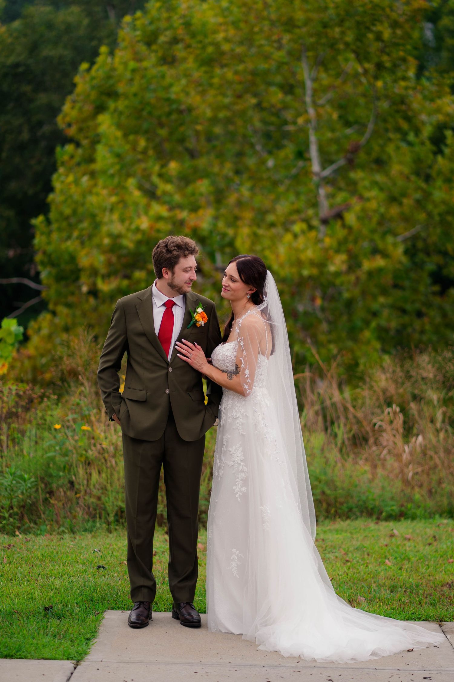 Bride and groom gaze at each other on a garden path surrounded by lush autumn foliage.