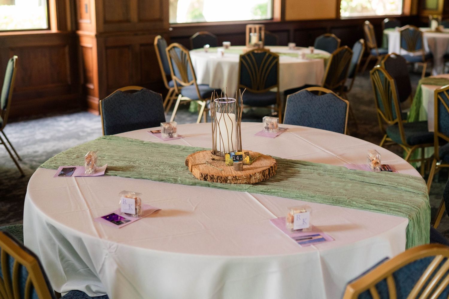 Elegant wedding reception table with green runner, wood slice centerpiece, and pink linens.
