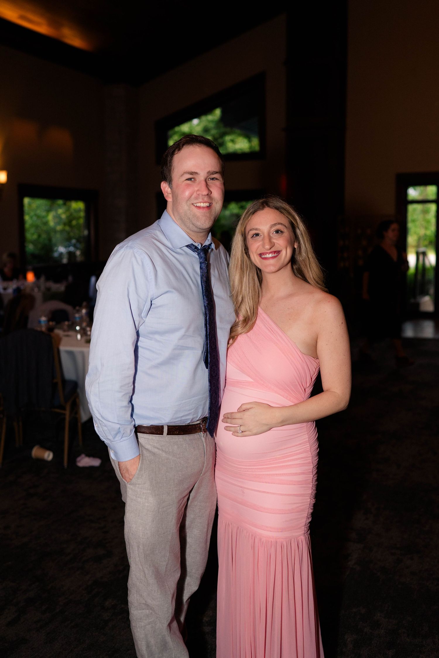 Smiling couple poses together at wedding reception, woman wearing pink one-shoulder gown.