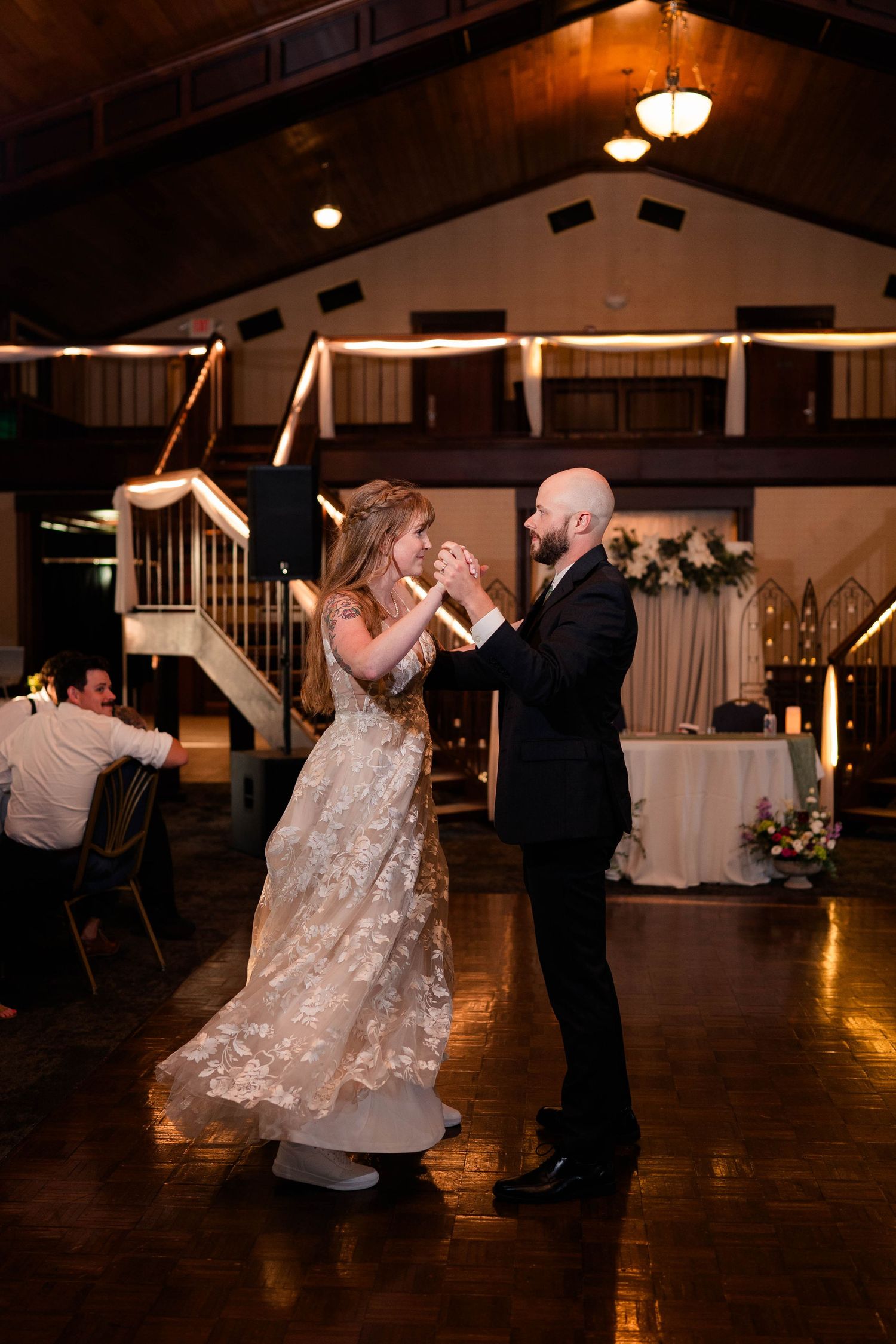 Bride and groom share romantic first dance in warmly lit rustic wedding reception hall.