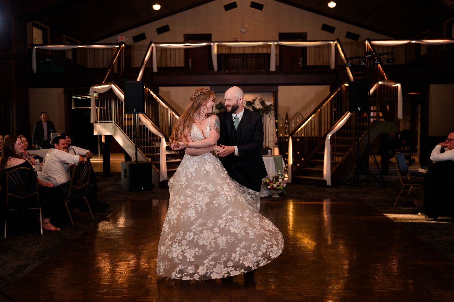 Bride in lace gown spins gracefully with groom during first dance at warmly lit wedding reception.