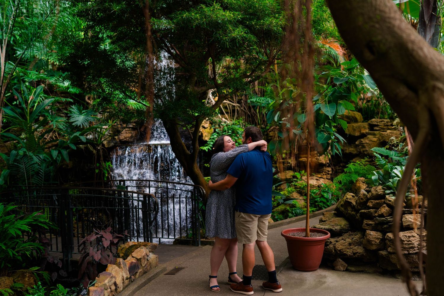 Couple embracing near a lush indoor waterfall surrounded by tropical greenery and rocks.