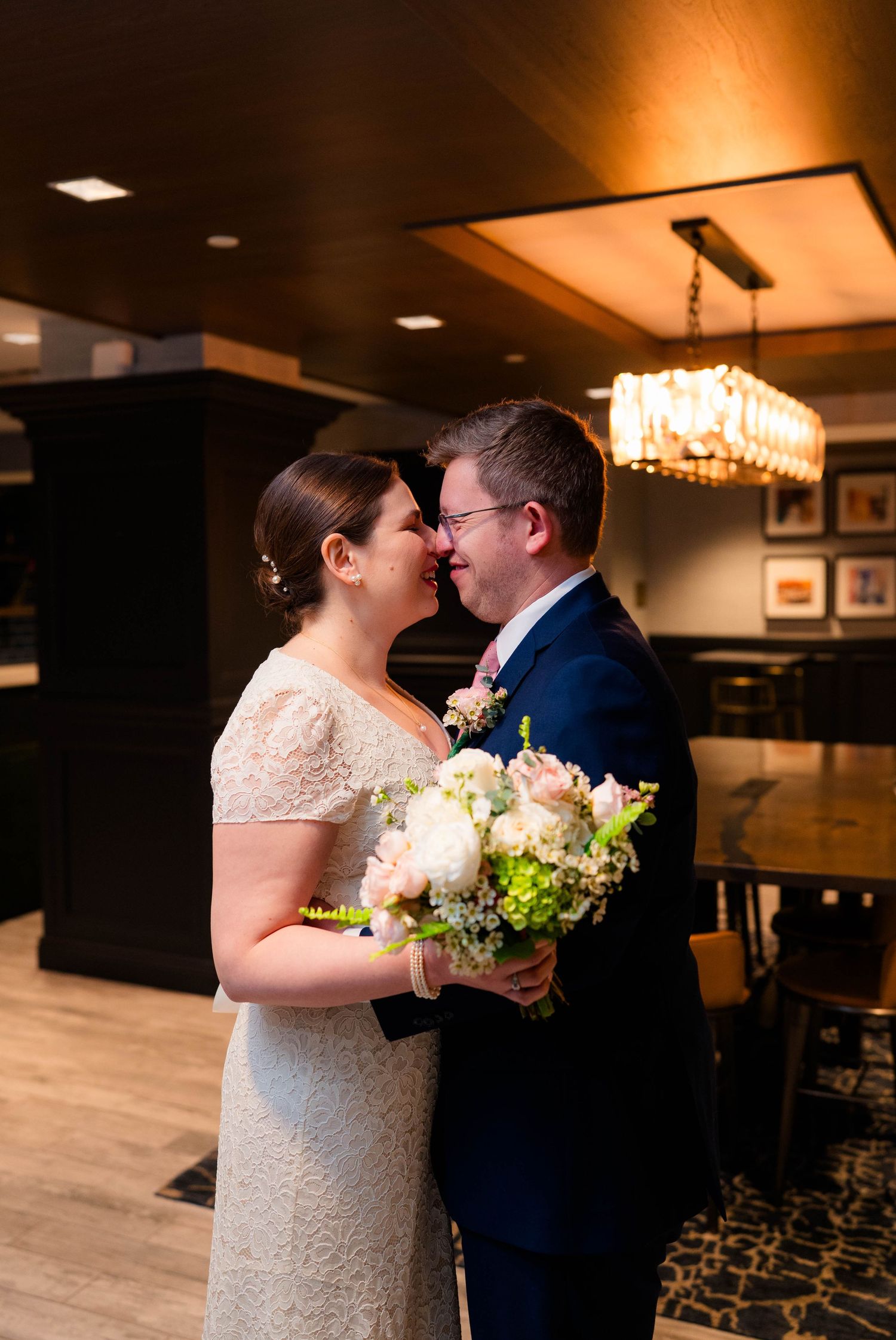 Bride and groom share an intimate nose-to-nose moment holding a pink and white floral bouquet.