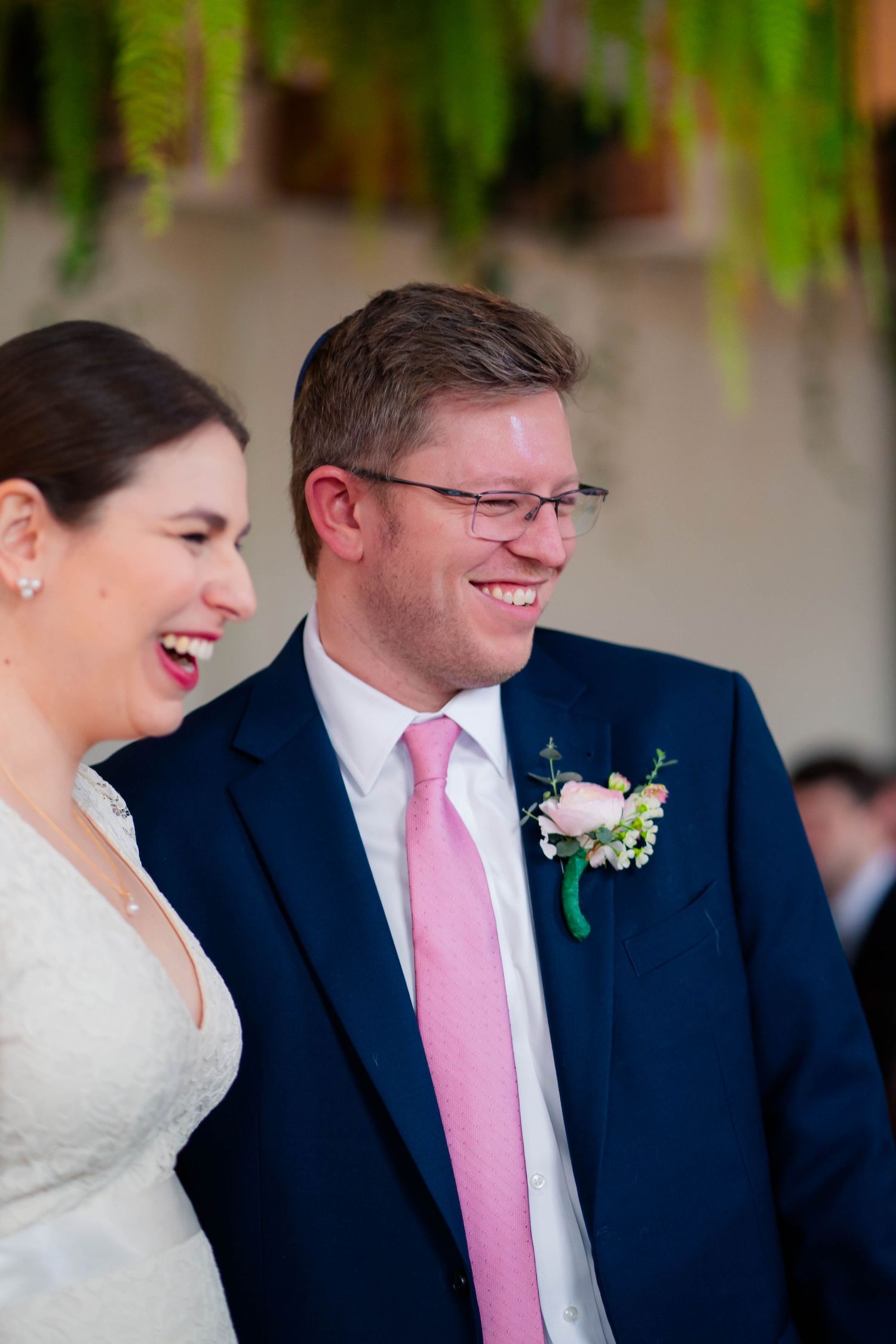 Smiling bride and groom laugh together during wedding ceremony, groom wearing pink boutonniere.