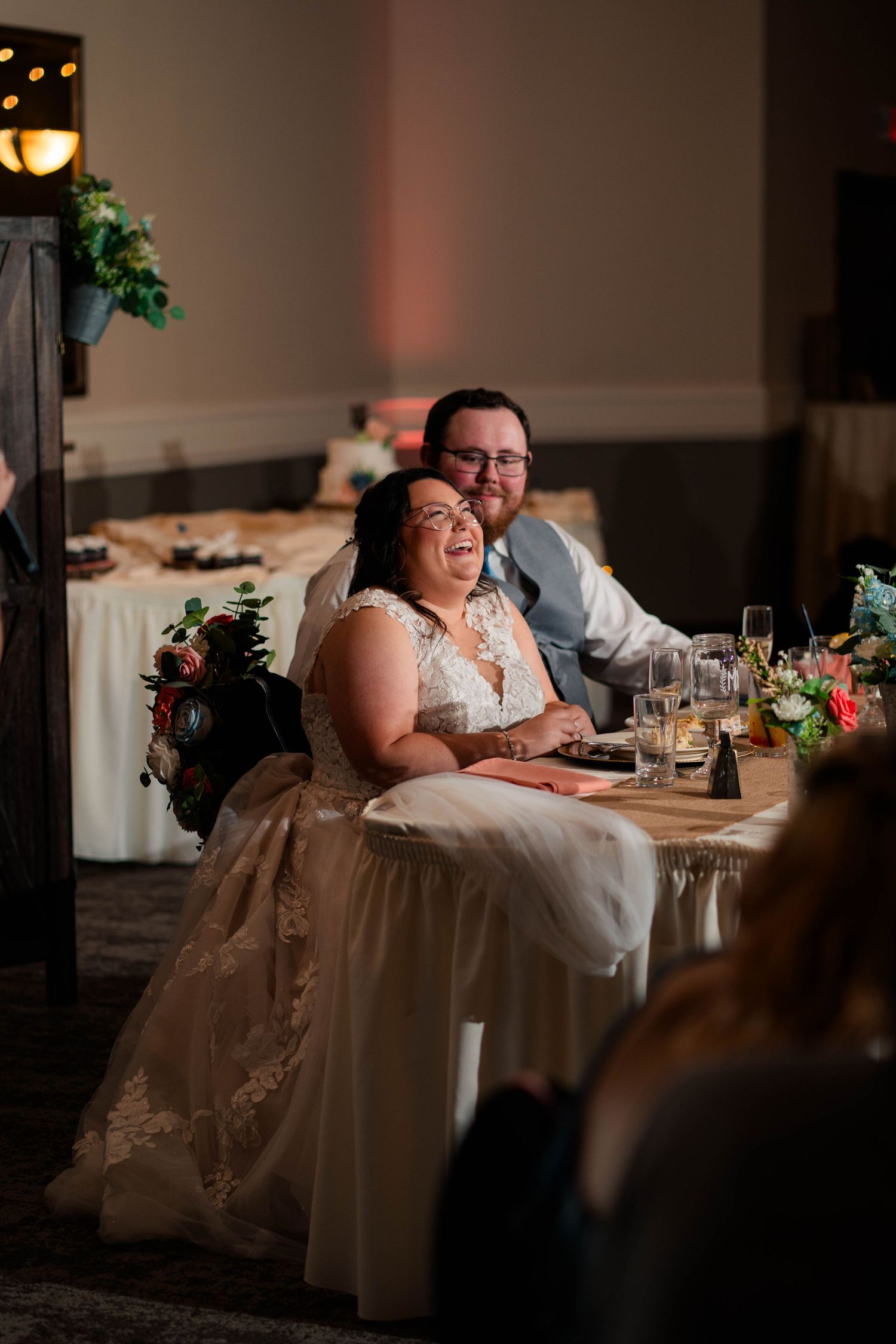 Bride and groom laughing together at sweetheart table during elegant wedding reception.