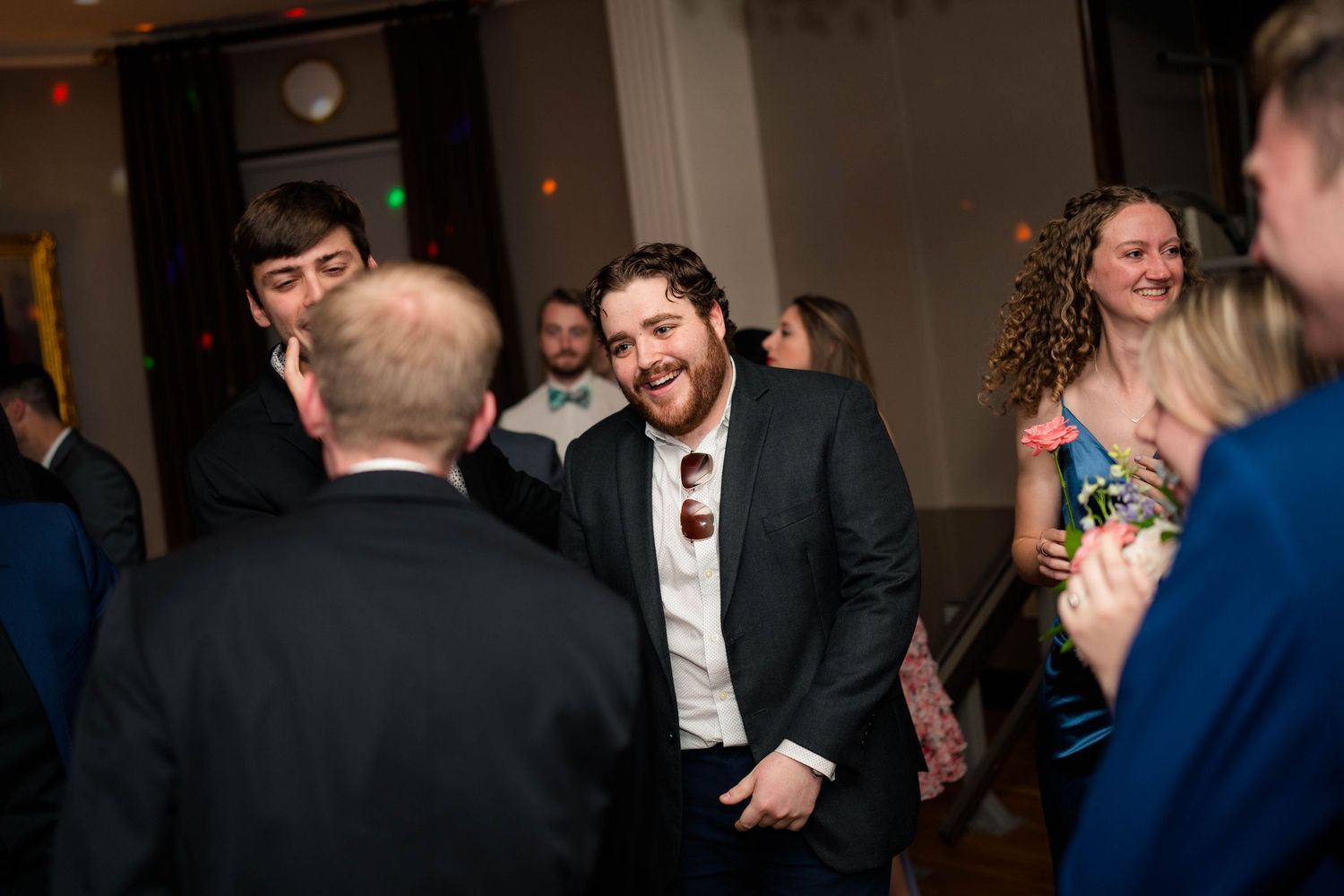 Cheerful wedding guest in dark suit laughs and dances at a lively indoor wedding reception.