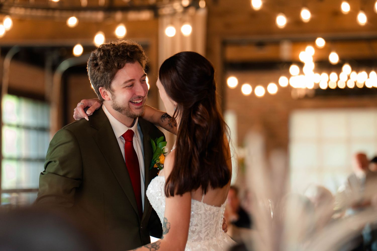 Bride whispers to groom as they share a joyful moment together under warm string lights at their reception.