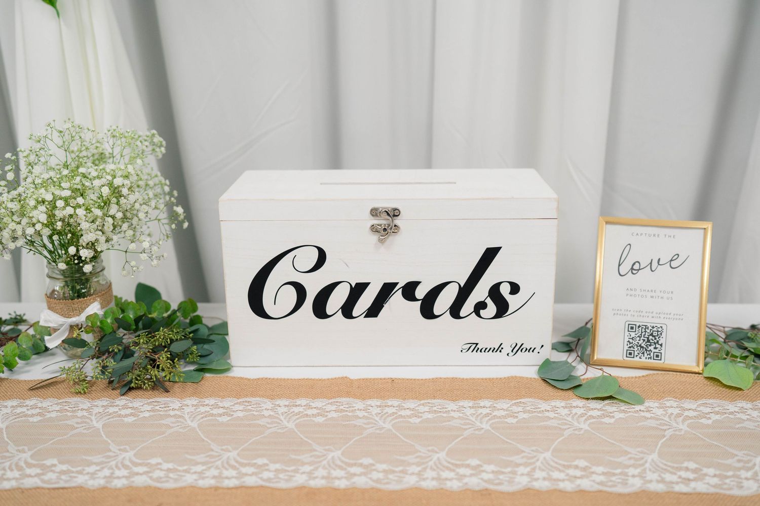 White wedding card box with Cards script lettering displayed on a burlap and lace table runner.