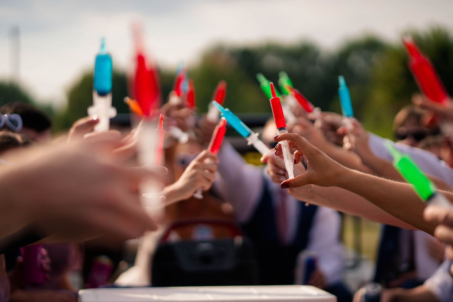 Wedding guests hold colorful glow sticks during outdoor celebration sendoff ceremony.