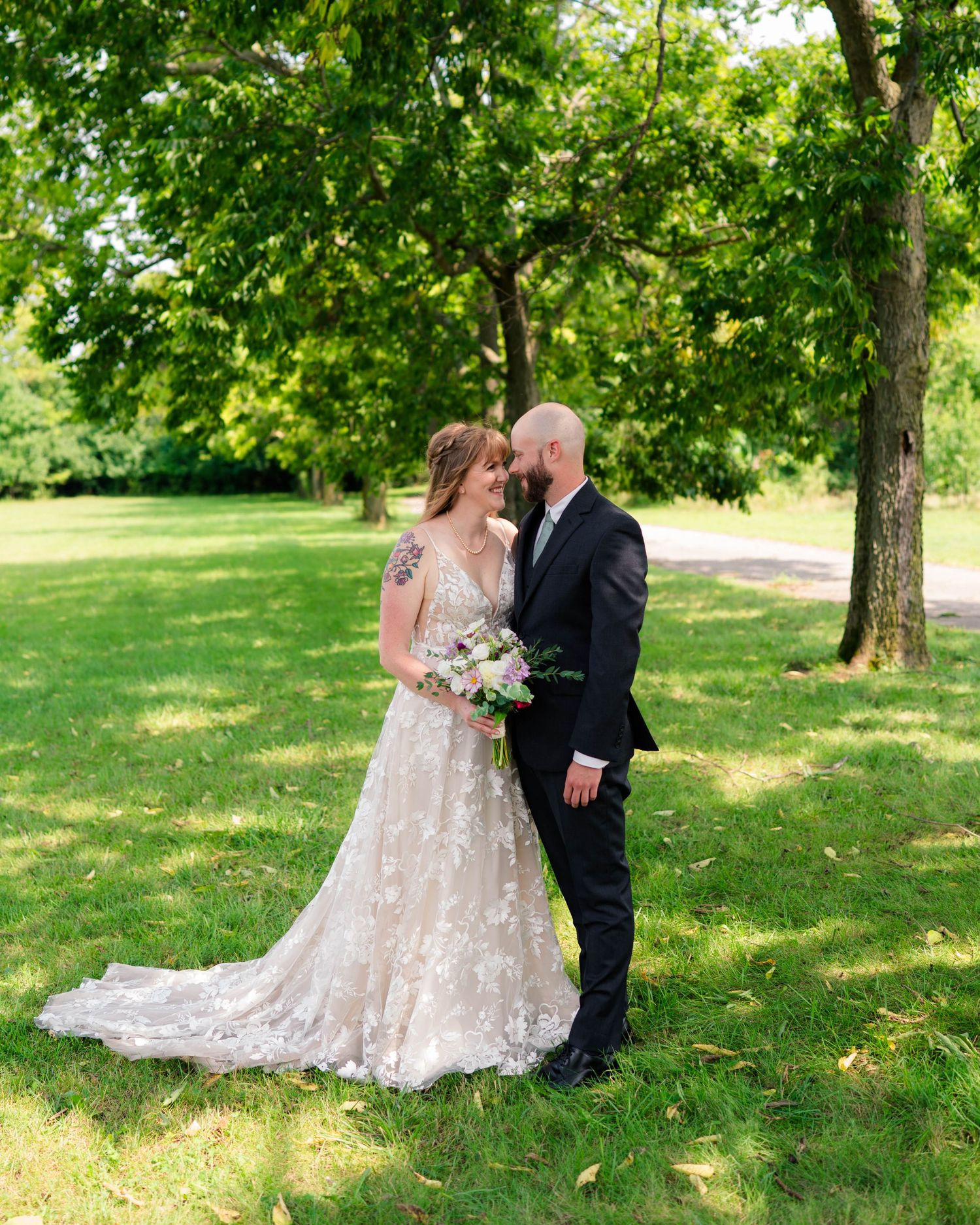 Bride and groom touch foreheads romantically in green park holding wedding bouquet.