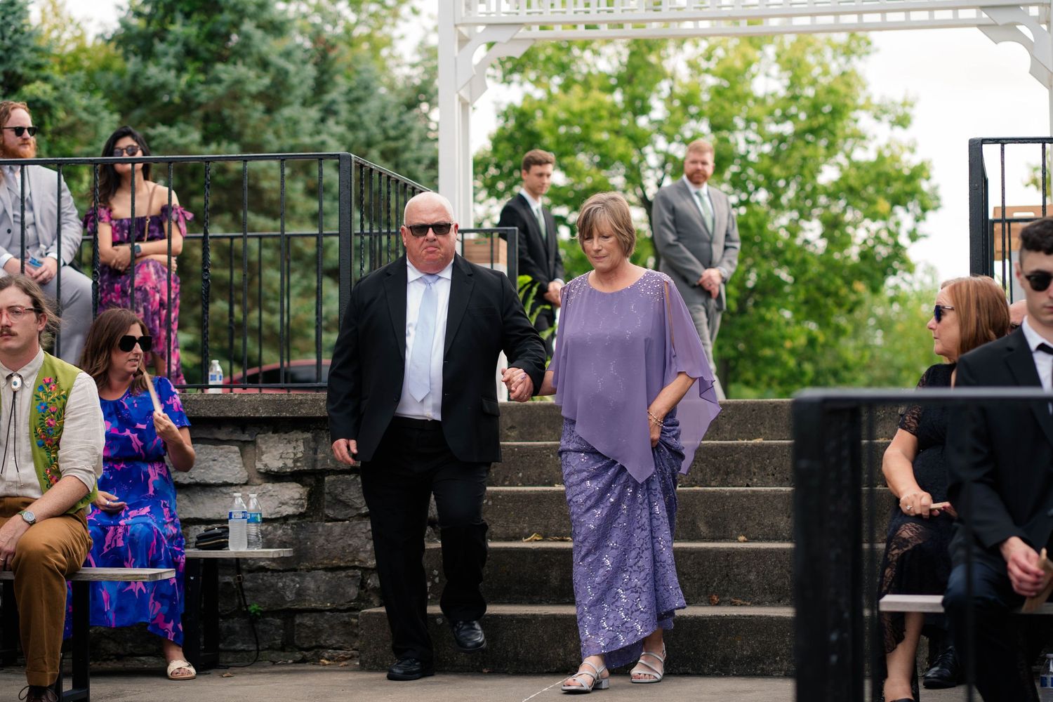 Elegantly dressed wedding guests descend outdoor stairs at a garden ceremony venue.