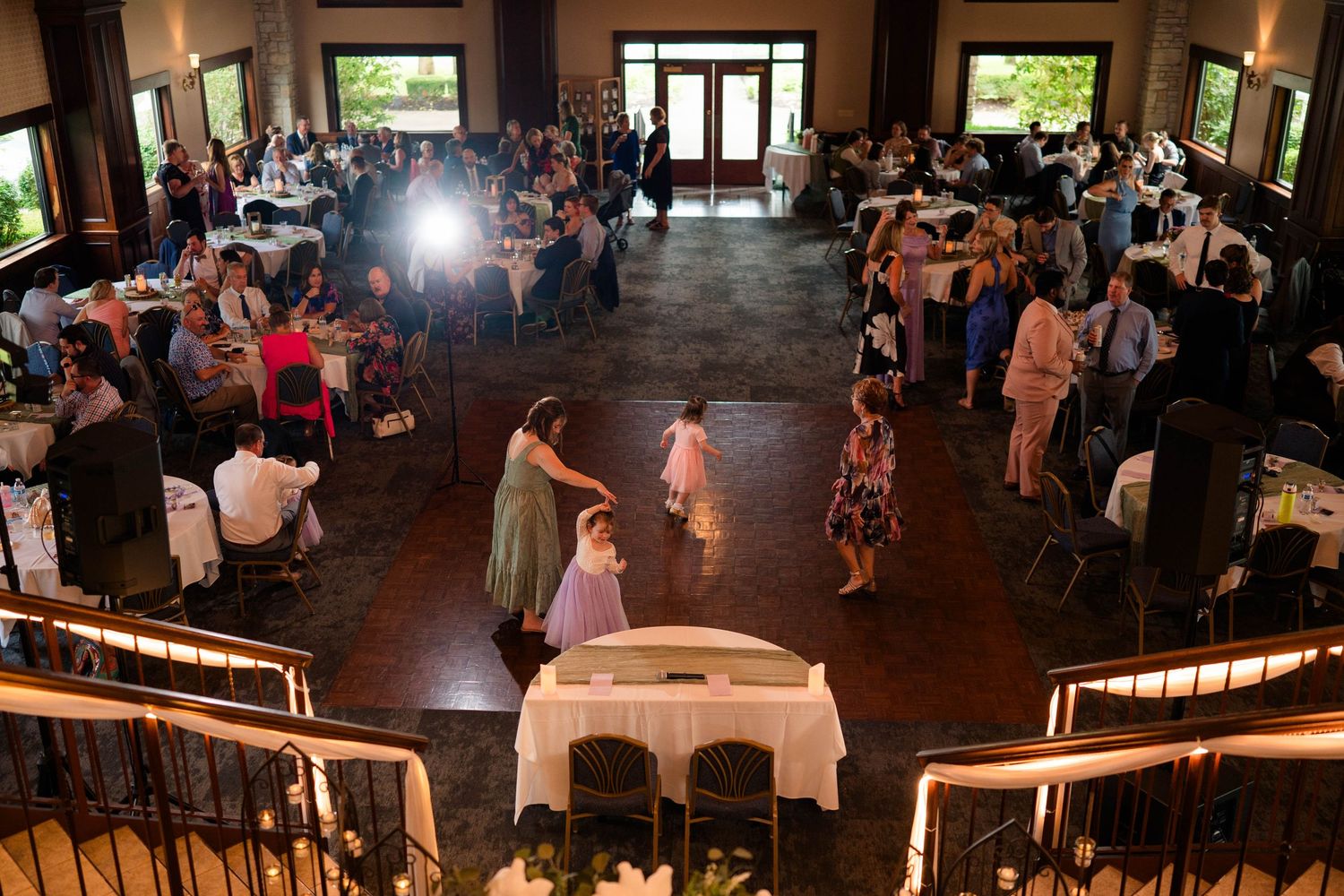 Aerial view of lively wedding reception with guests dancing and mingling in a rustic venue.