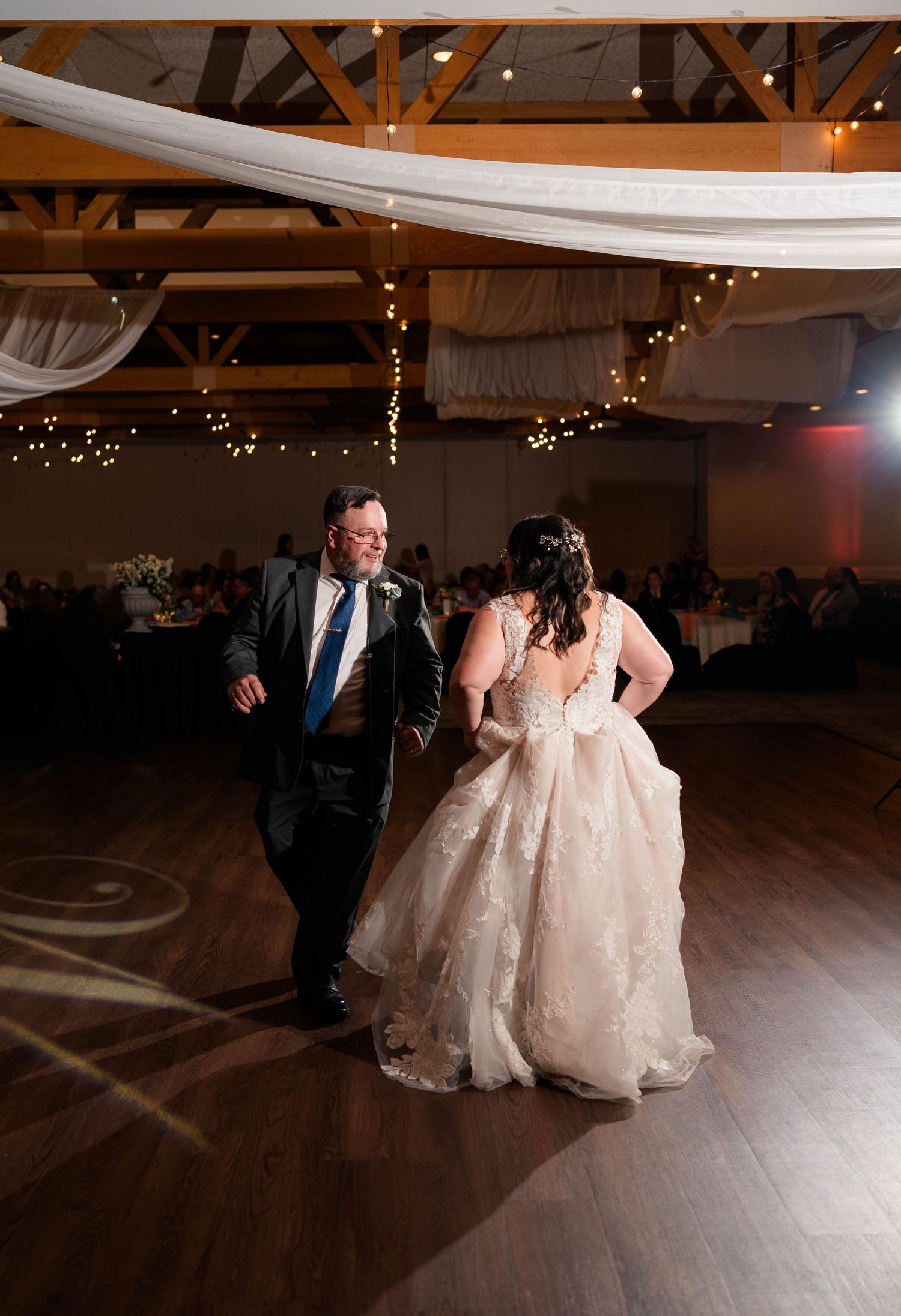Father escorts bride onto decorated wedding reception dance floor for father-daughter dance.