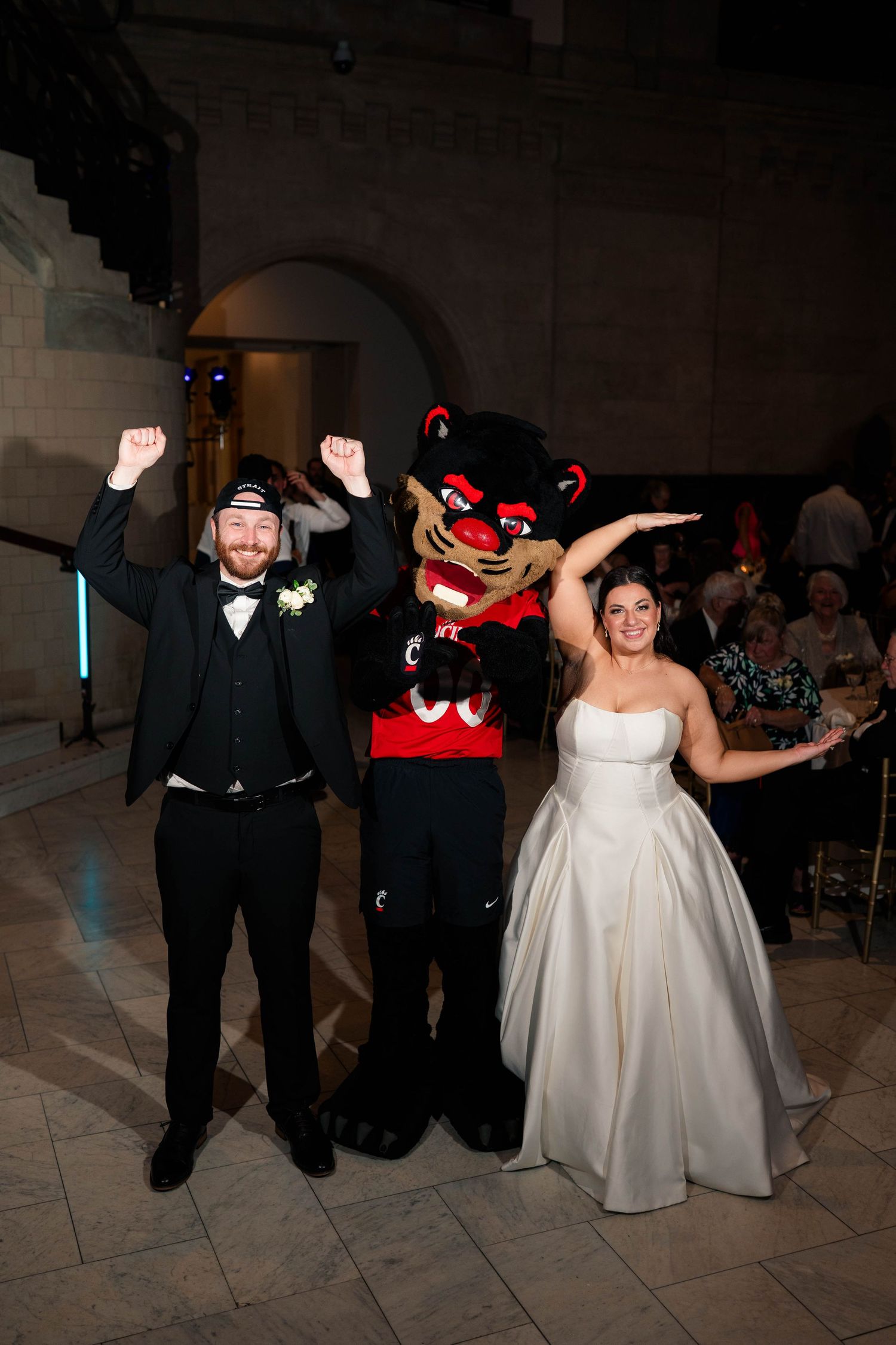 Bride and groom pose with university mascot costume character at their fun wedding reception celebration.