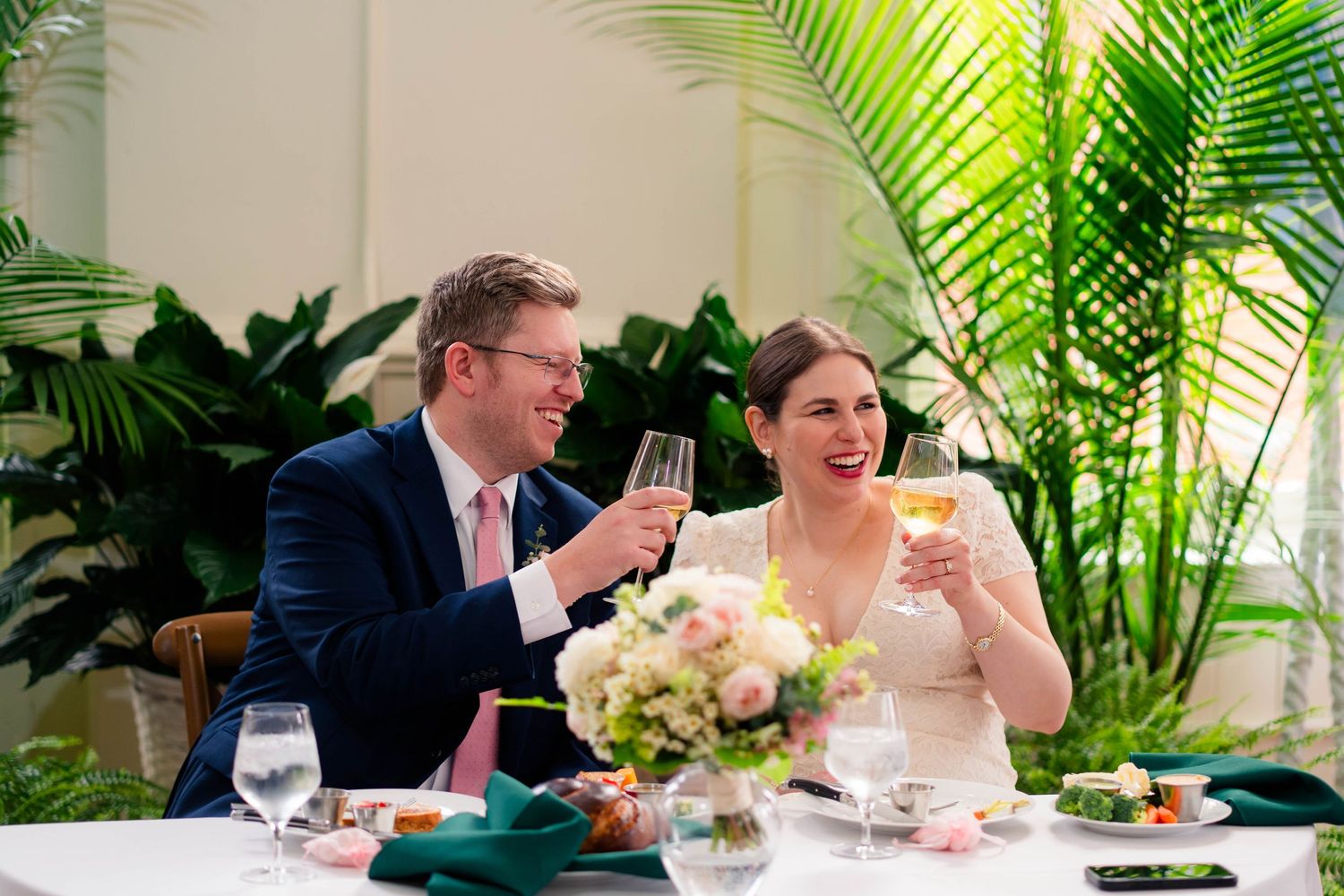 Happy bride and groom toasting with champagne glasses at their floral-decorated wedding reception table.