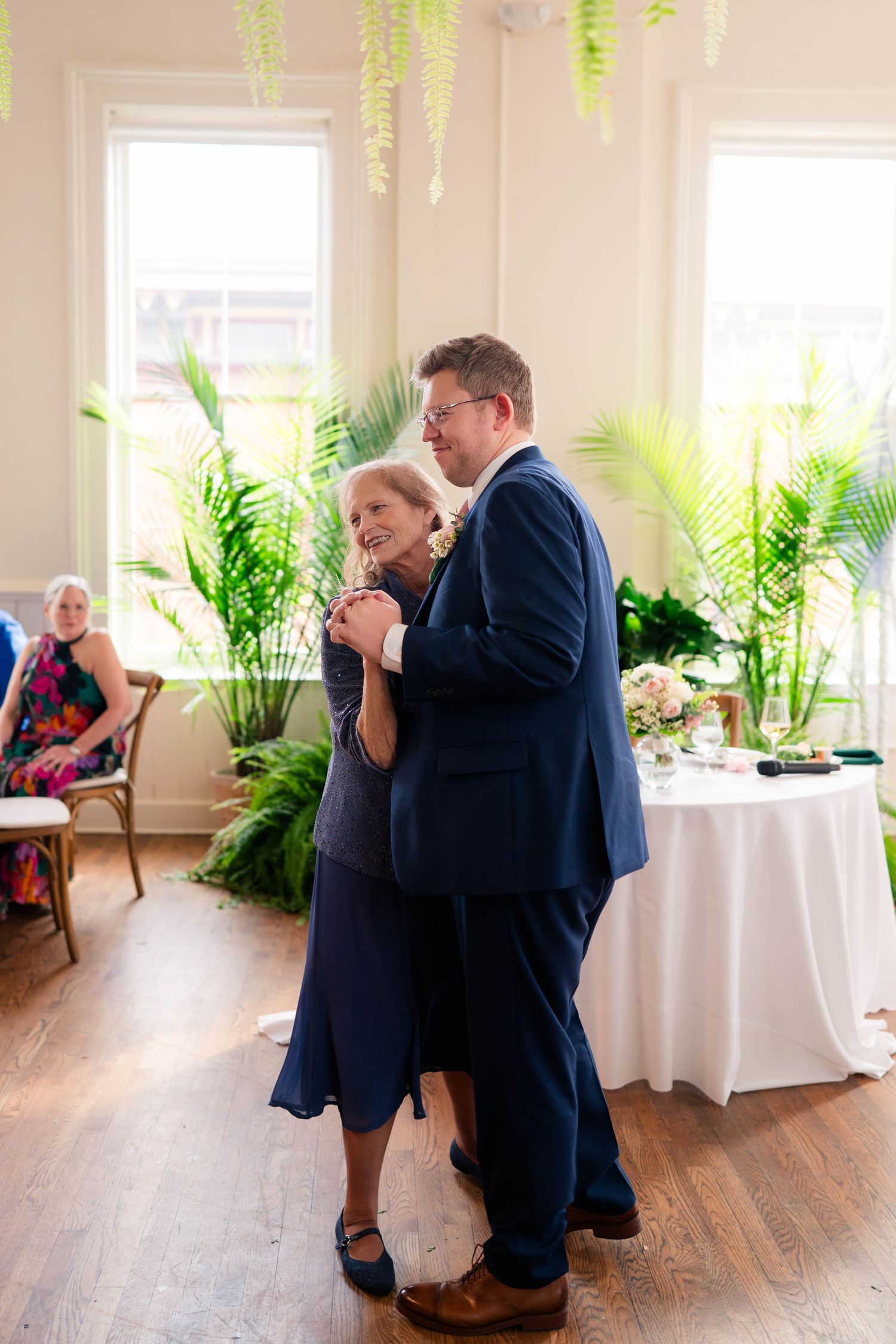 Groom in navy suit and mother in blue dress share tender mother-son wedding dance.