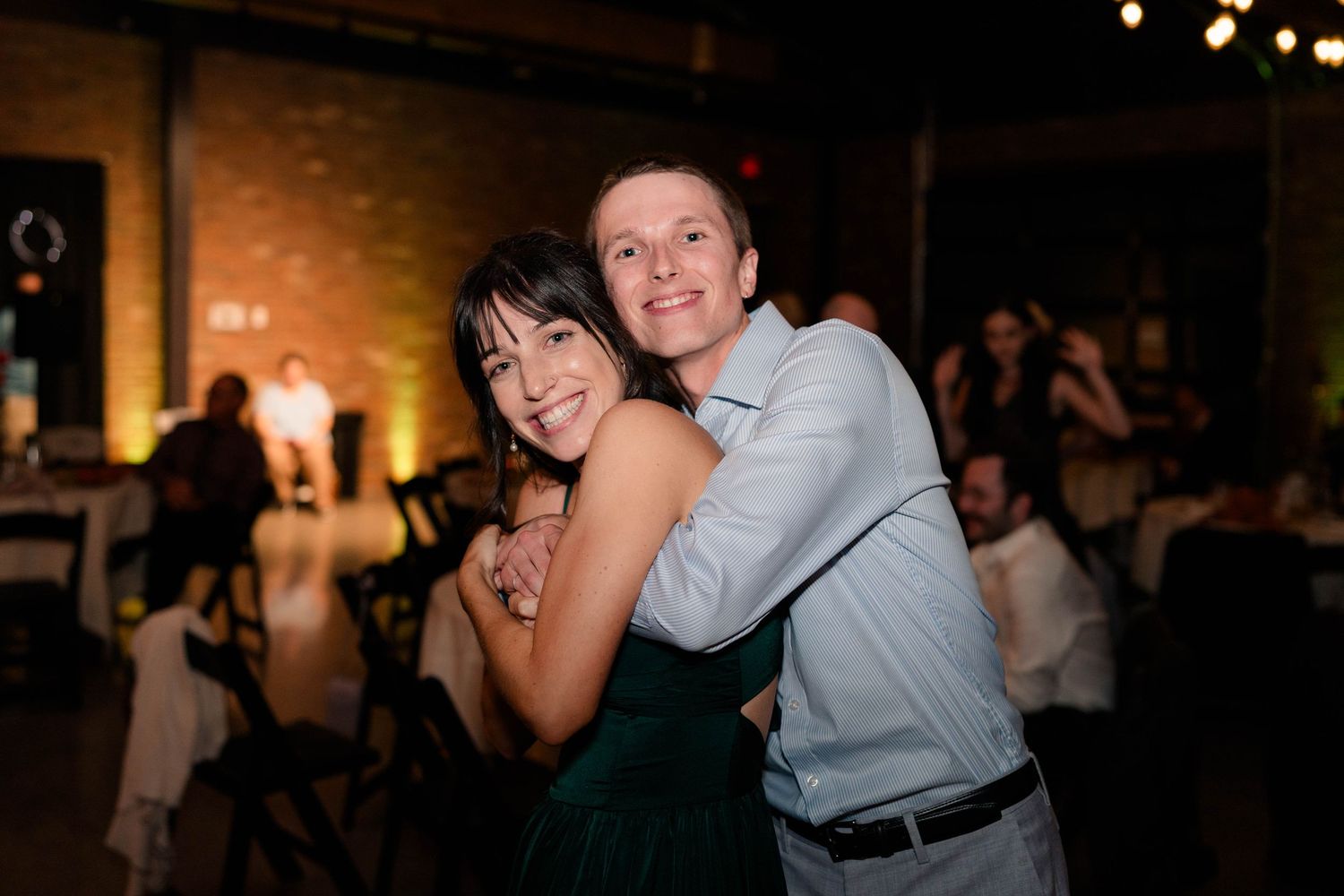 Smiling couple poses together at wedding reception in warmly lit rustic venue.