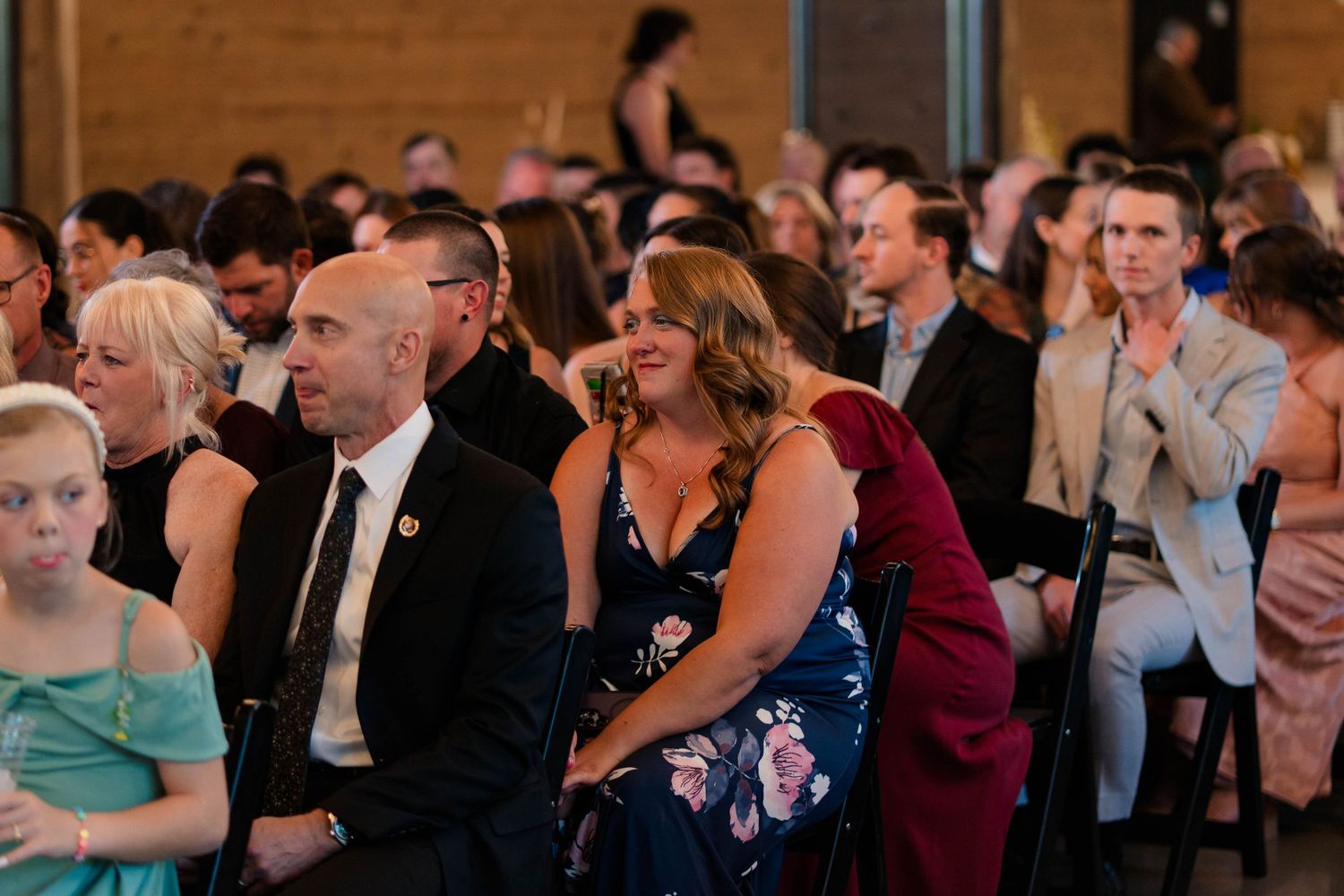 Wedding guests smile and watch the ceremony from their seats inside an elegant venue.