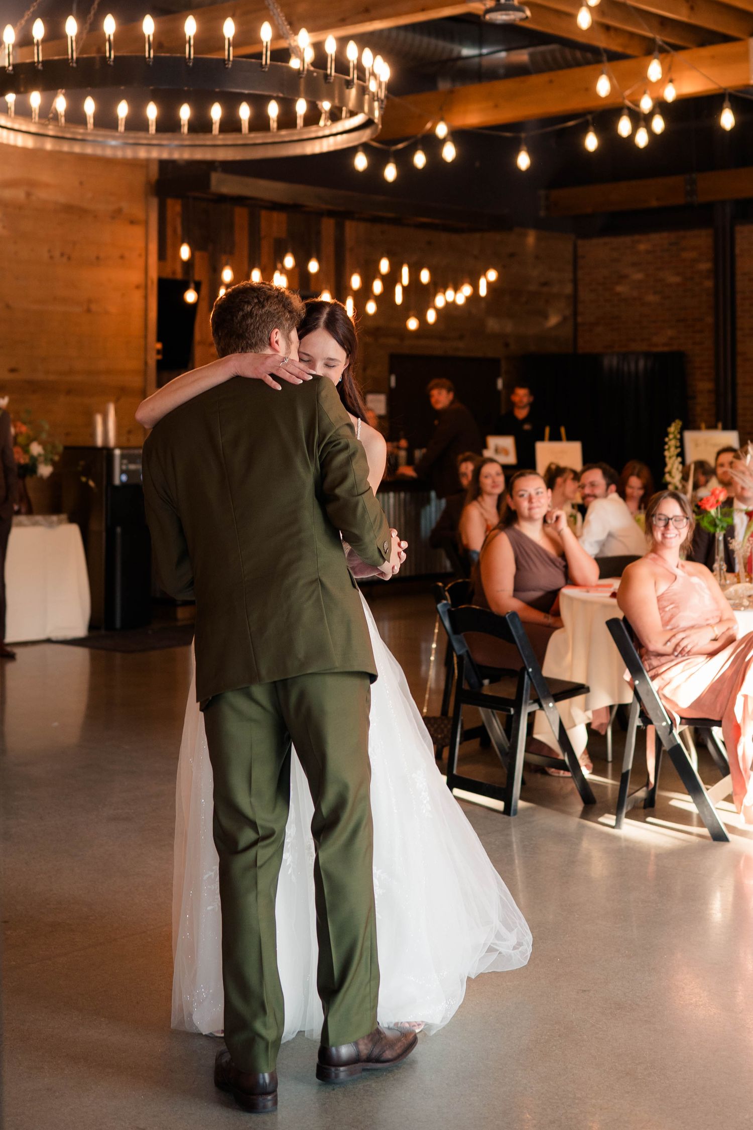Couple sharing emotional first dance under chandelier lights at wedding reception.