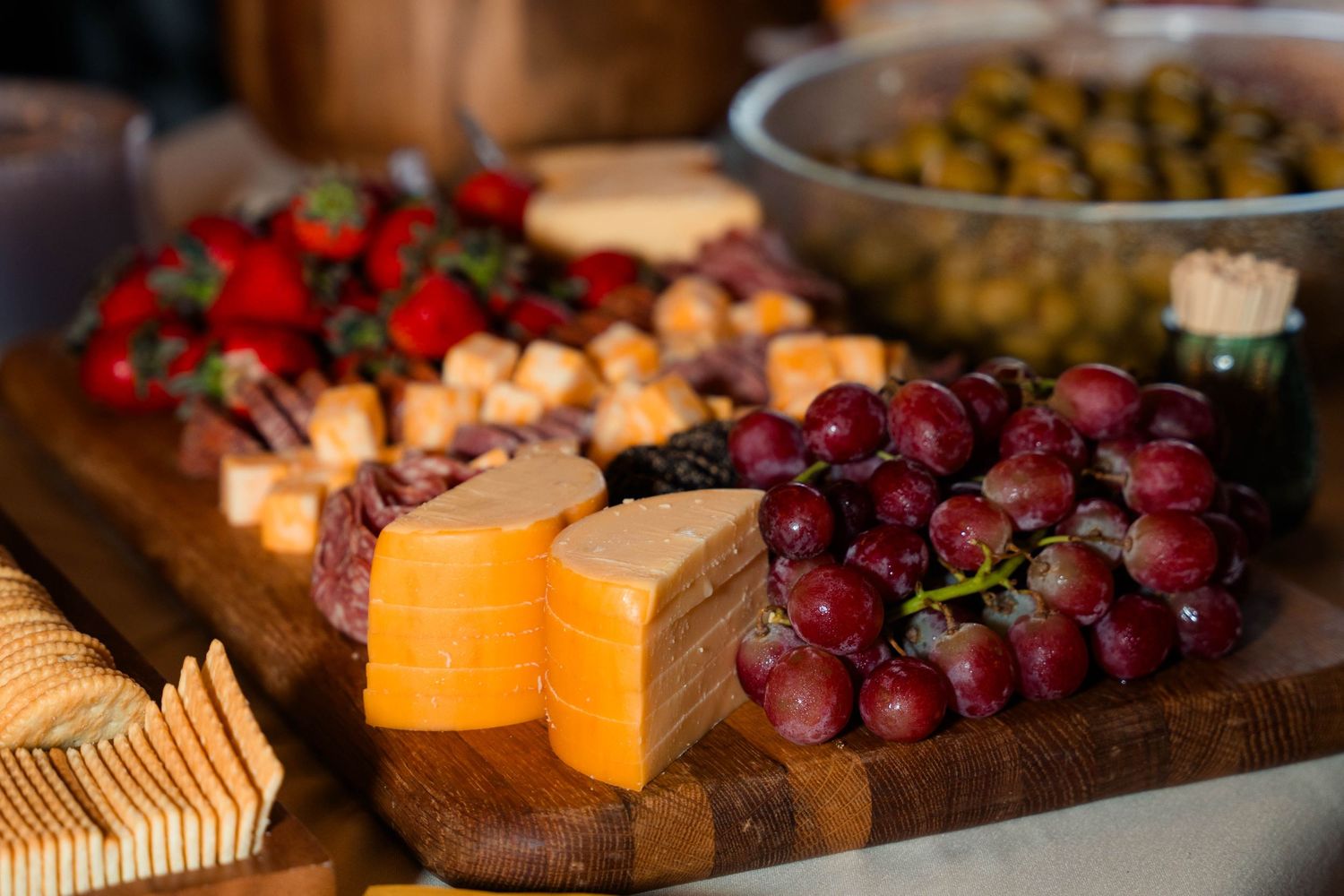Elegant charcuterie board with grapes, strawberries, cheese cubes, crackers, and olives at wedding reception.
