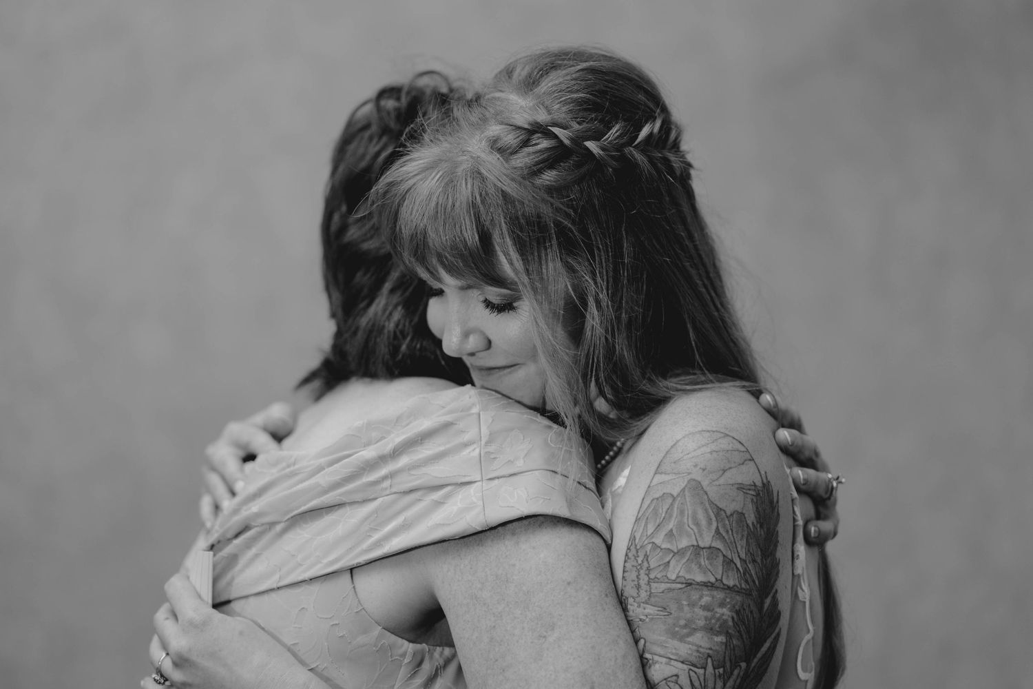 A tattooed bride shares an emotional hug with a loved one in a tender black and white photo.