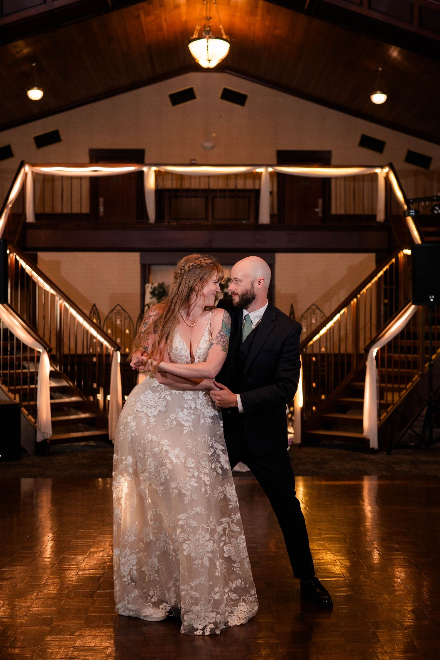 Bride and groom share romantic first dance beneath warm lights in rustic elegant wedding reception venue.