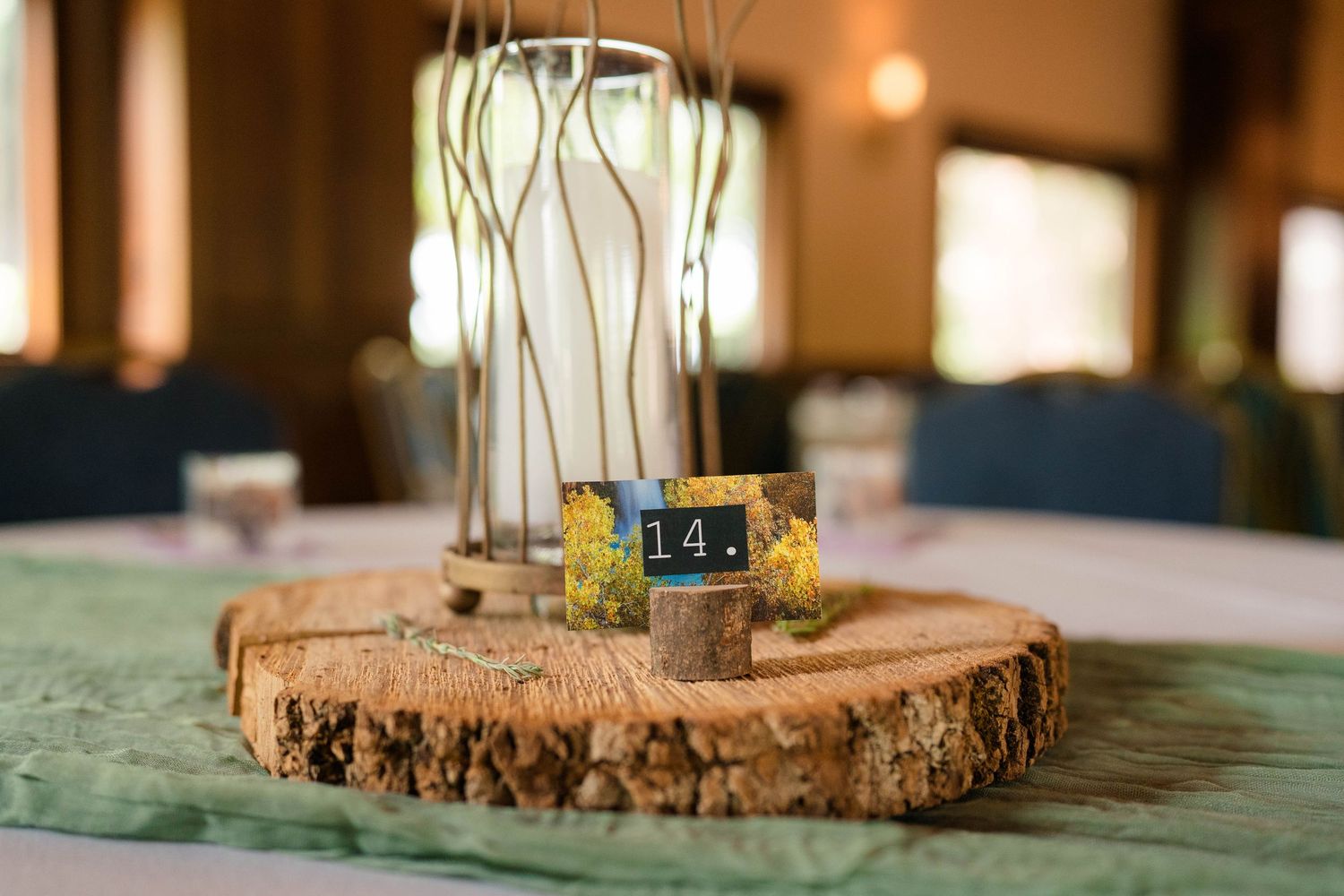 Rustic wedding centerpiece with wood slice base, table number 14, and glass cylinder vase with branches.
