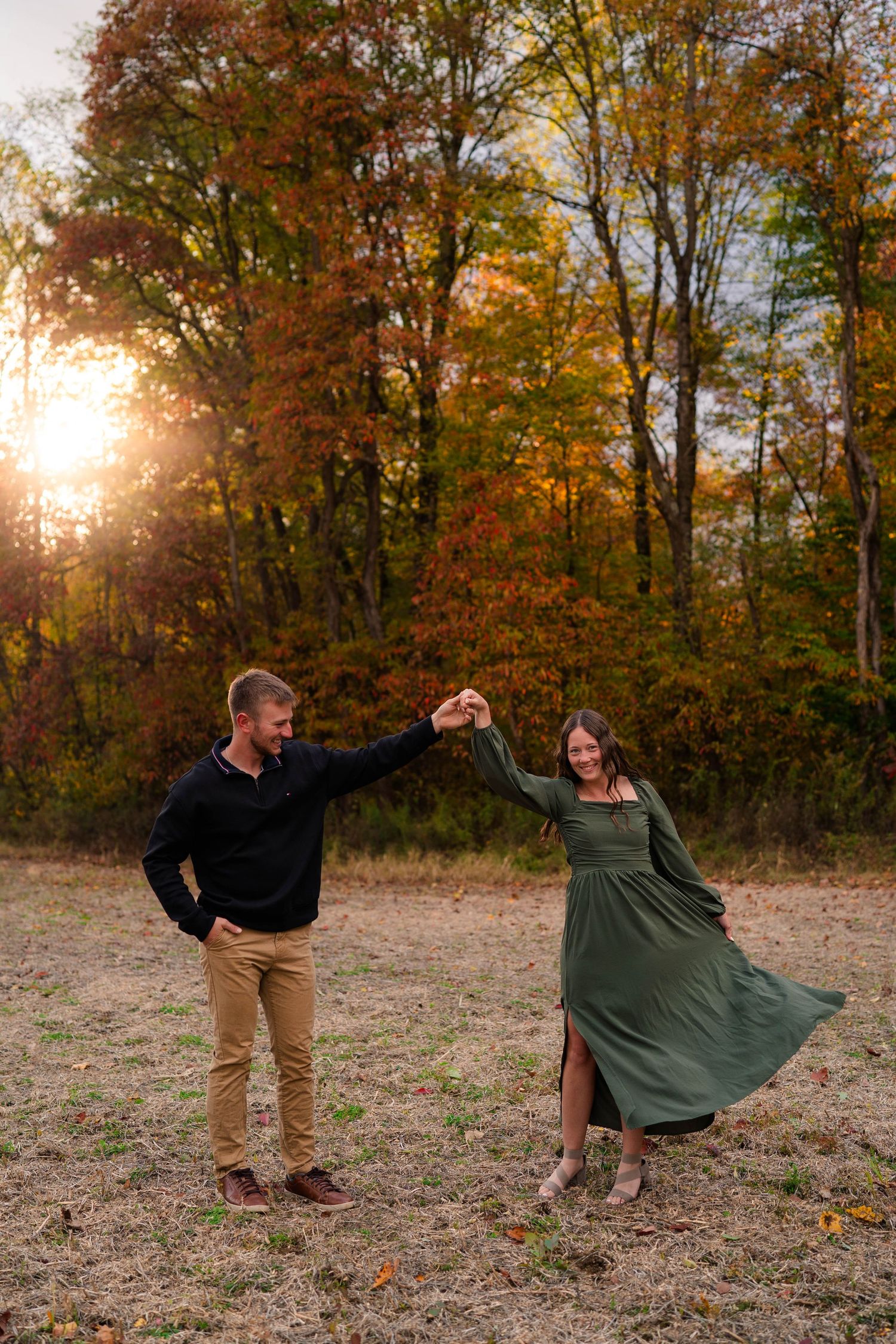 Couple dancing together in autumn field at golden hour, woman in green dress twirling.