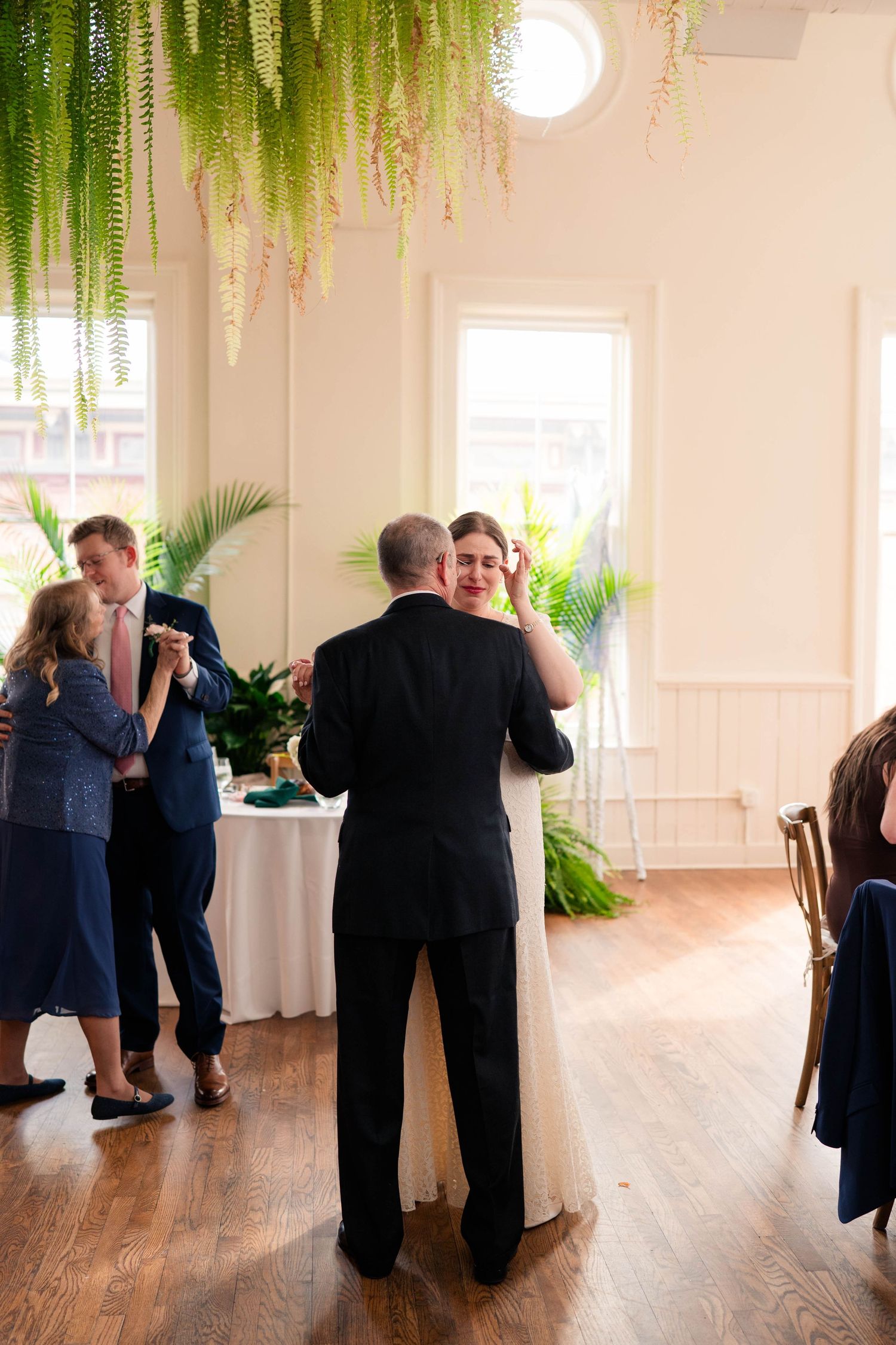 Bride and father dancing while groom and mother share mother-son dance at reception.