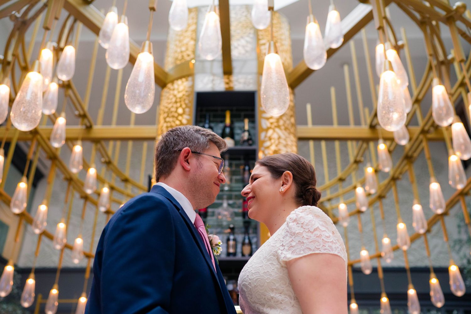 Bride and groom share a romantic moment under elegant gold chandeliers with teardrop lights at their wedding venue.