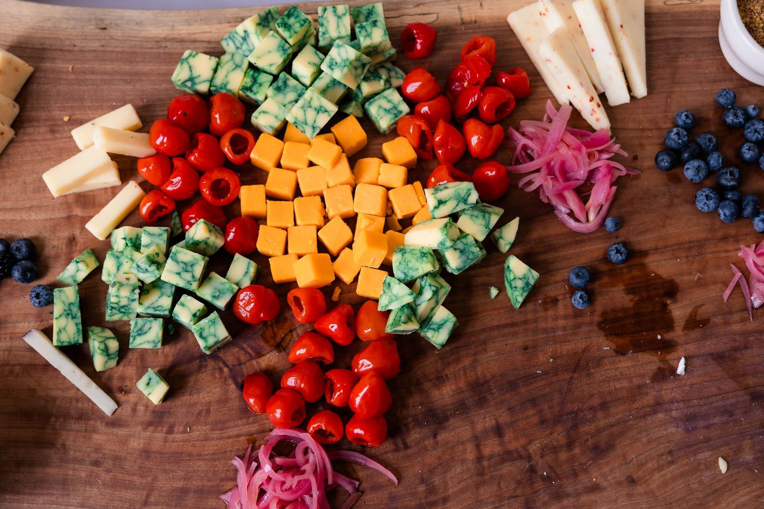 Colorful wedding charcuterie board with cherry tomatoes, cheddar, blueberries, and pickled onions.