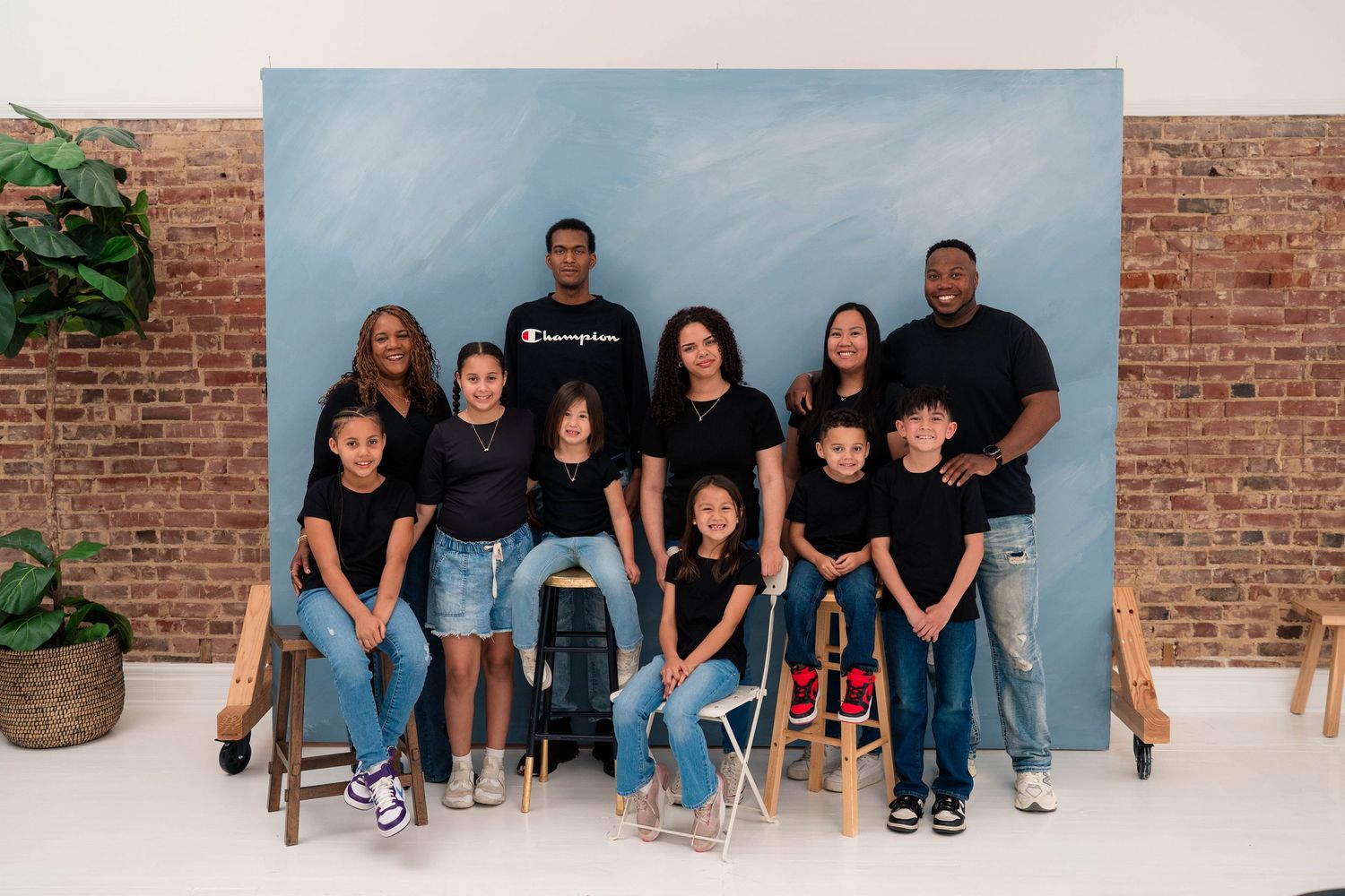 Large family group portrait with adults and children in black outfits posing in front of a blue backdrop.