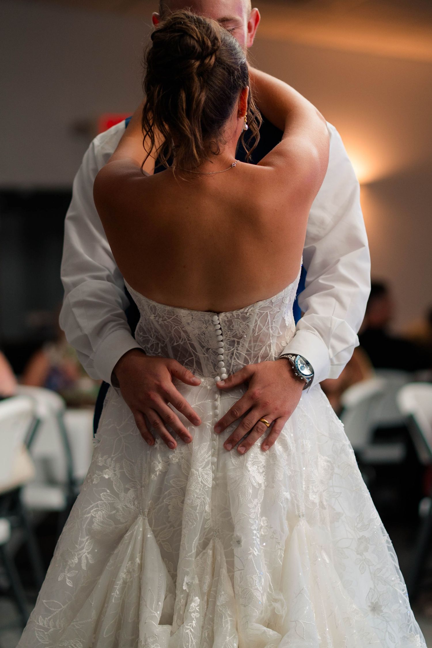 Back view of bride in backless lace wedding gown dancing with groom at reception.