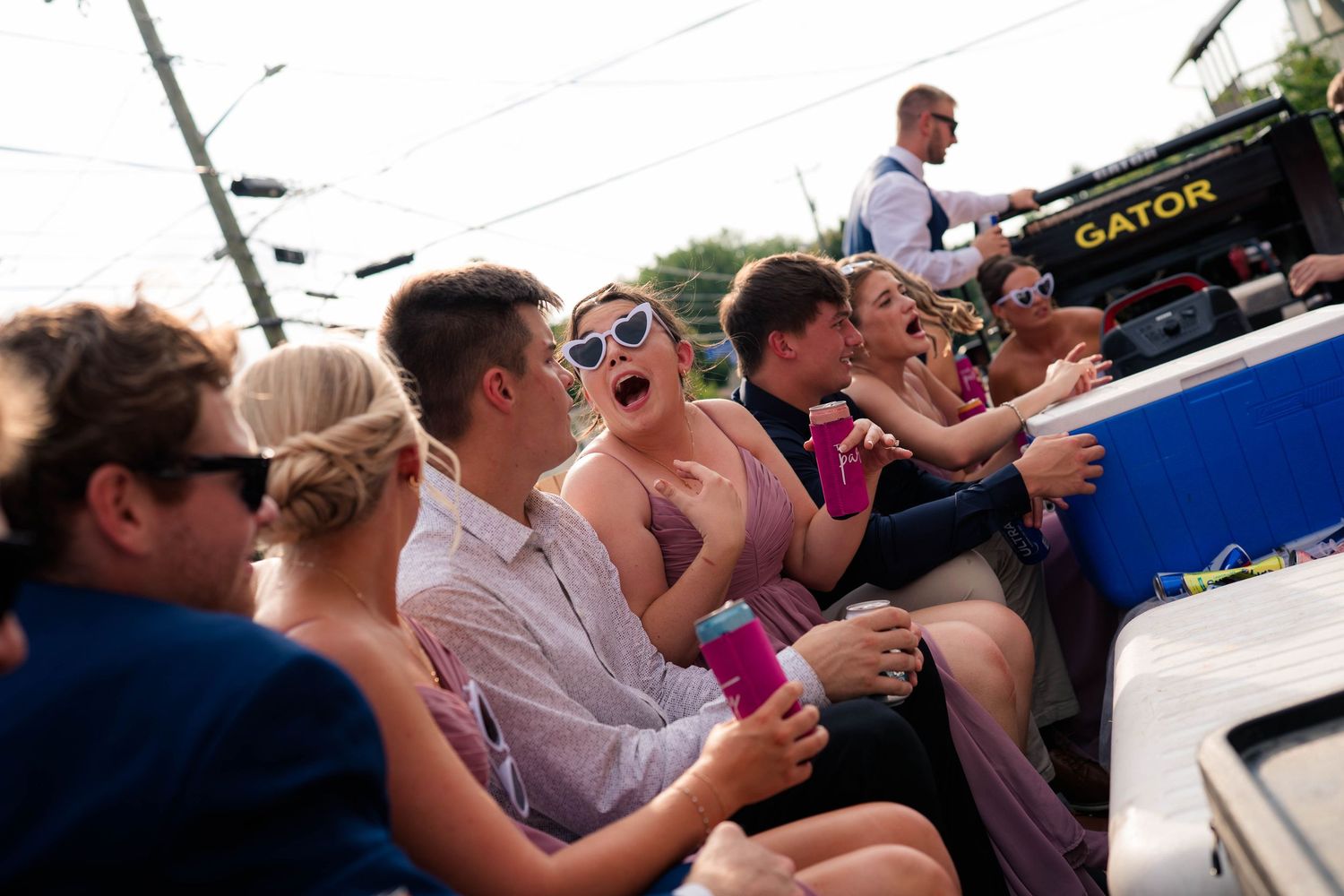 Wedding guests laughing and celebrating while riding together in an open utility vehicle outdoors.