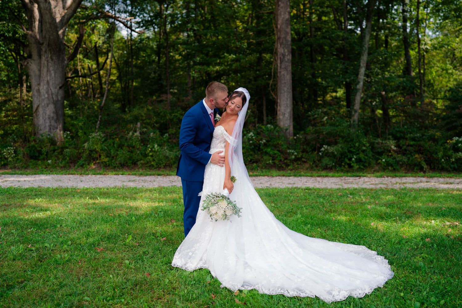 Bride and groom sharing romantic kiss in lush green outdoor setting on wedding day.