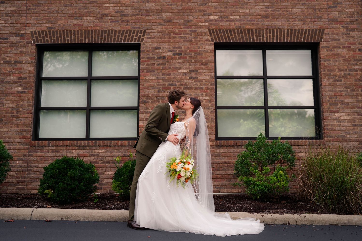 Bride and groom share a romantic kiss outside a brick building on their wedding day.