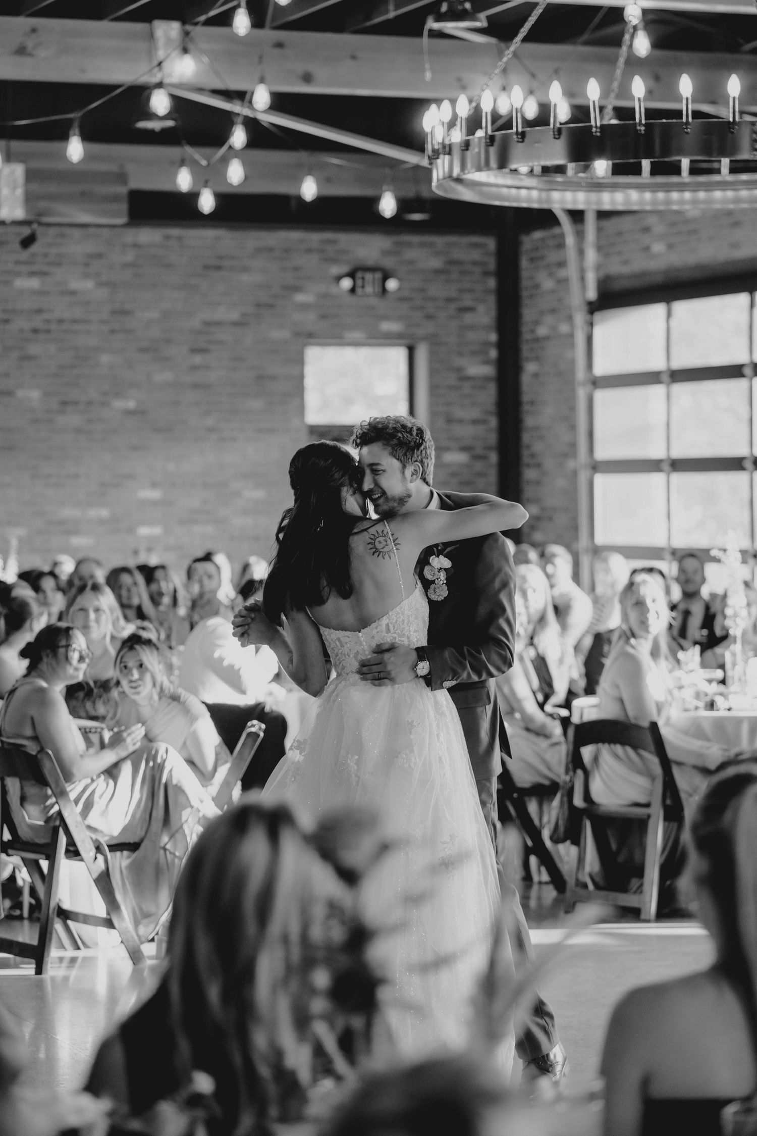 Black and white photo of bride and groom sharing first dance in rustic reception hall.