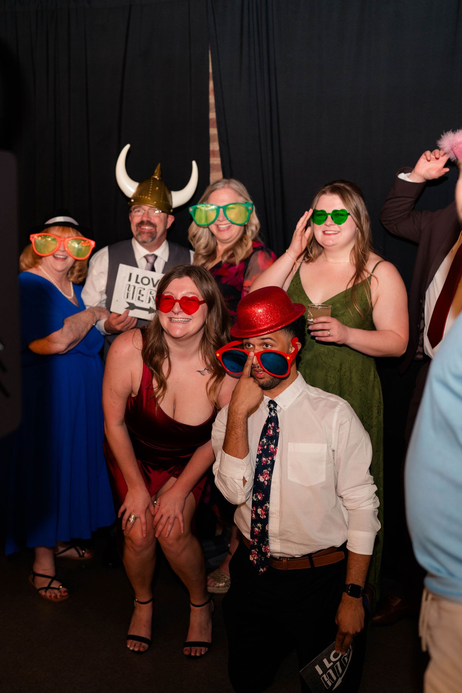 Wedding guests posing in photo booth with fun props including viking helmet and oversized sunglasses.