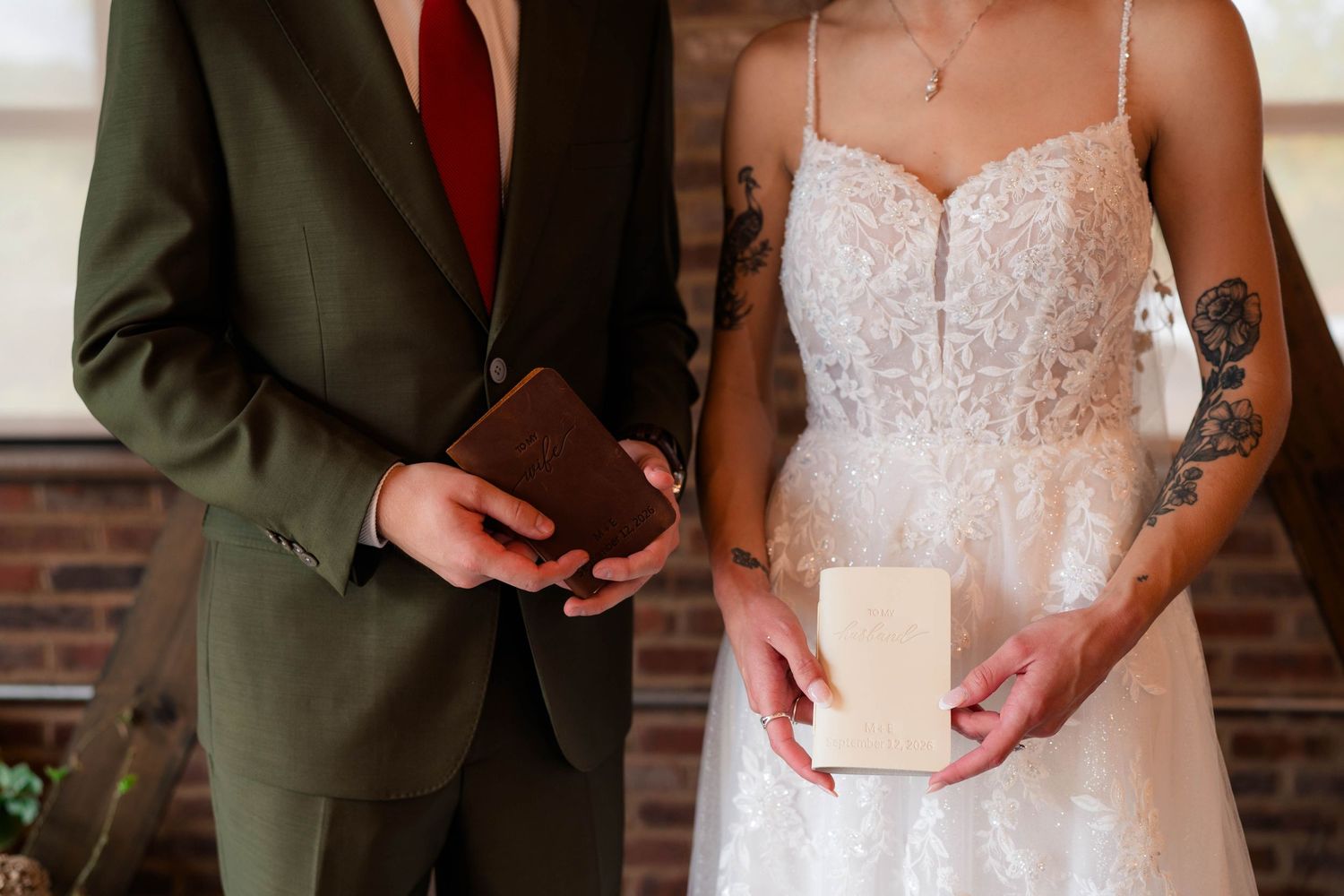 Bride and groom holding vow books during wedding ceremony in rustic brick venue.