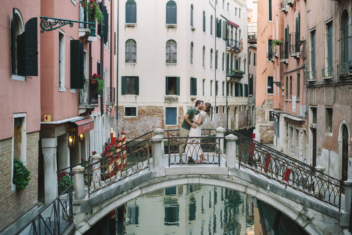 Romantic couple kissing on a stone bridge over a Venice canal surrounded by colorful buildings.